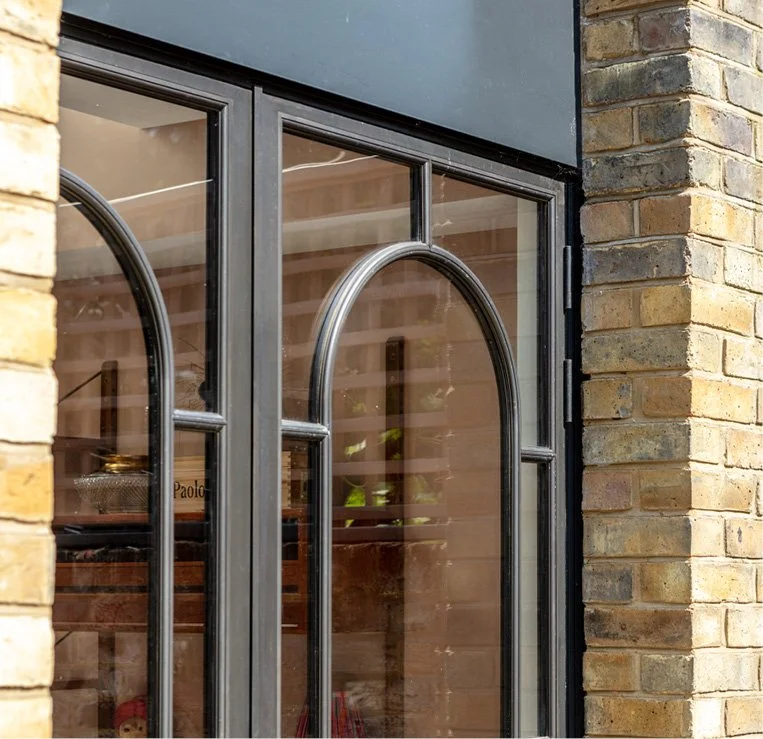 Close-up of a glass door with metal framing and arched design, set in a brick wall exterior.