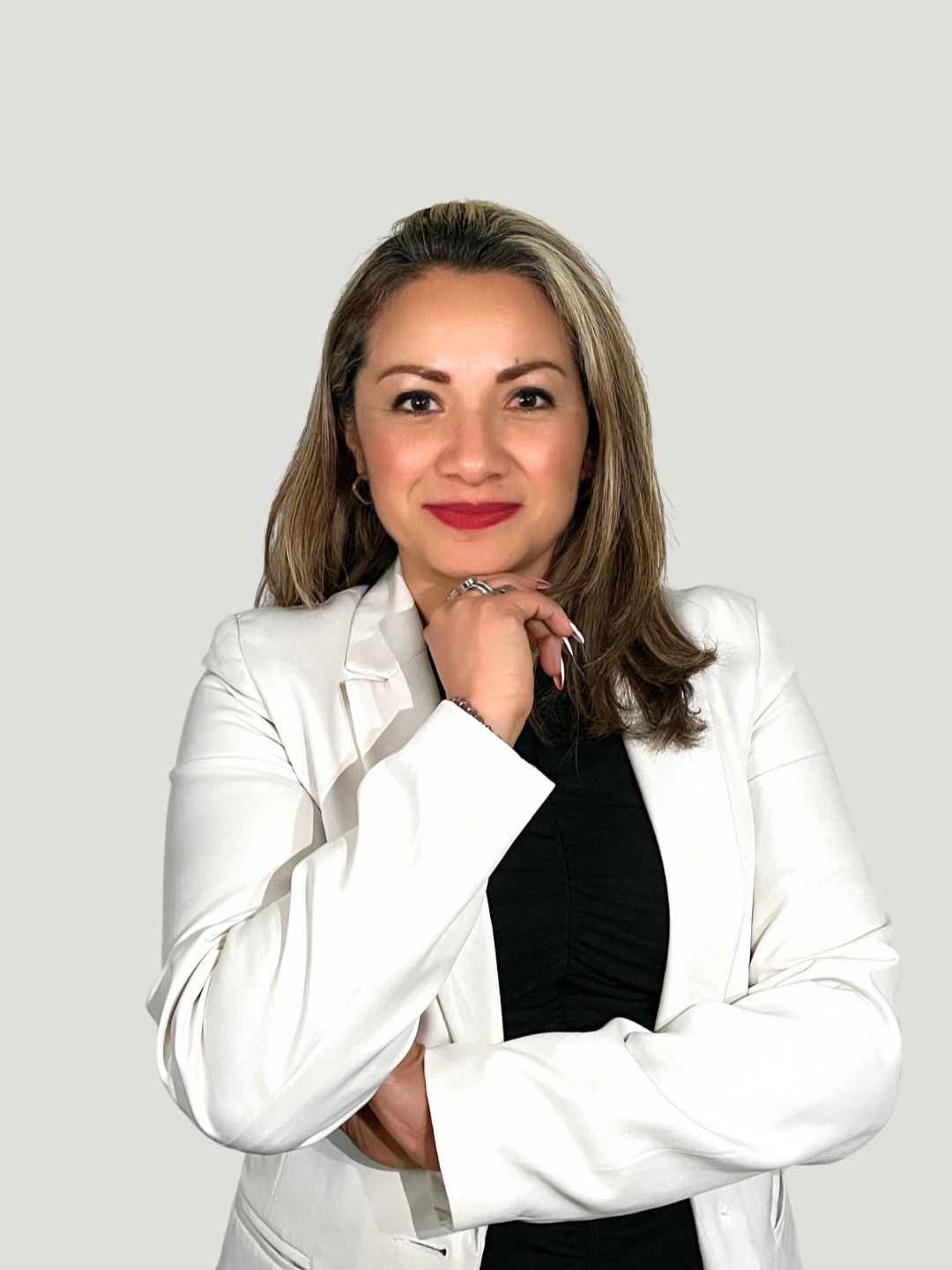 Mujer con cabello castaño claro, maquillaje rojo y ropa profesional, con la mano en el rostro, usando saco blanco, fondo gris