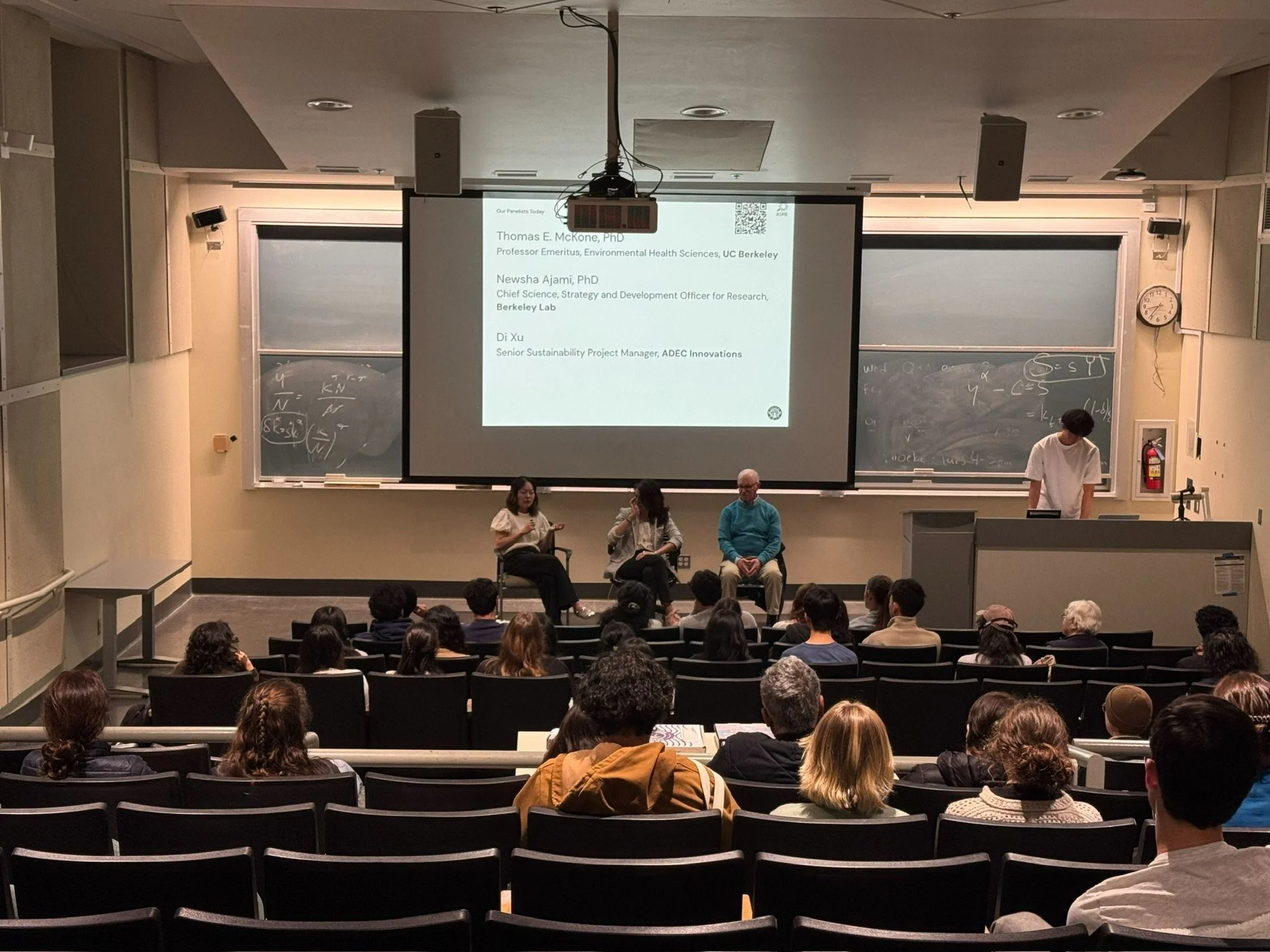 Three speakers on stage in front of an audience.