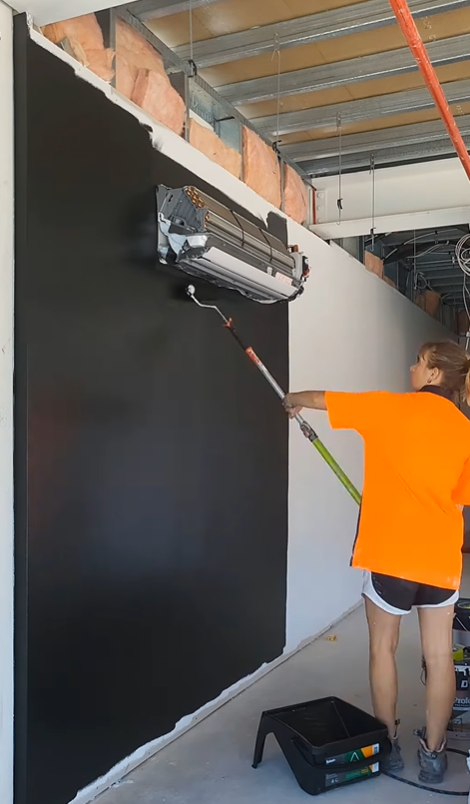 Person painting a black wall with a roller at a construction site.