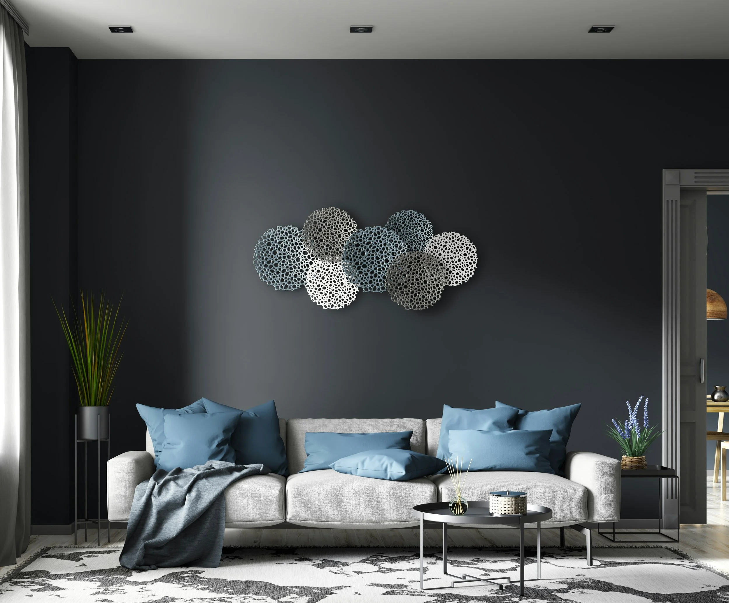 Living room with a dark gray wall, a light gray sofa with blue pillows, a black side table with potted lavender, a round coffee table with decorative items, a tall green plant, and modern wall art with overlapping circular patterns.