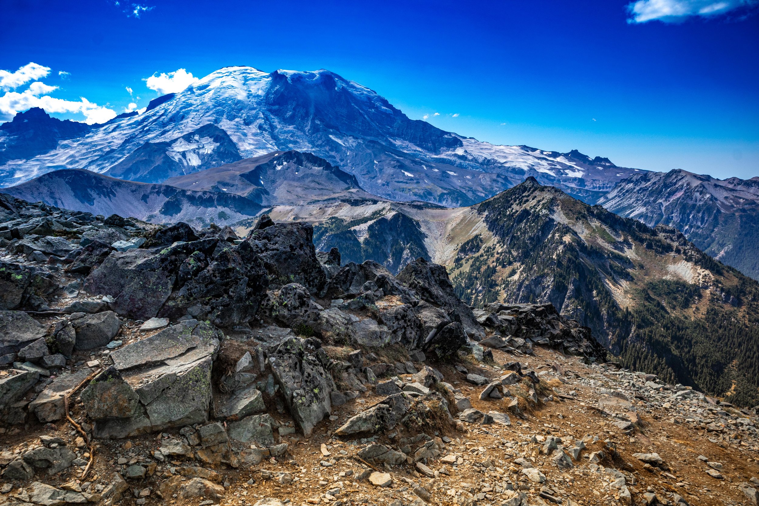 Mountain landscape with snow-capped peaks and rocky trail in the foreground.