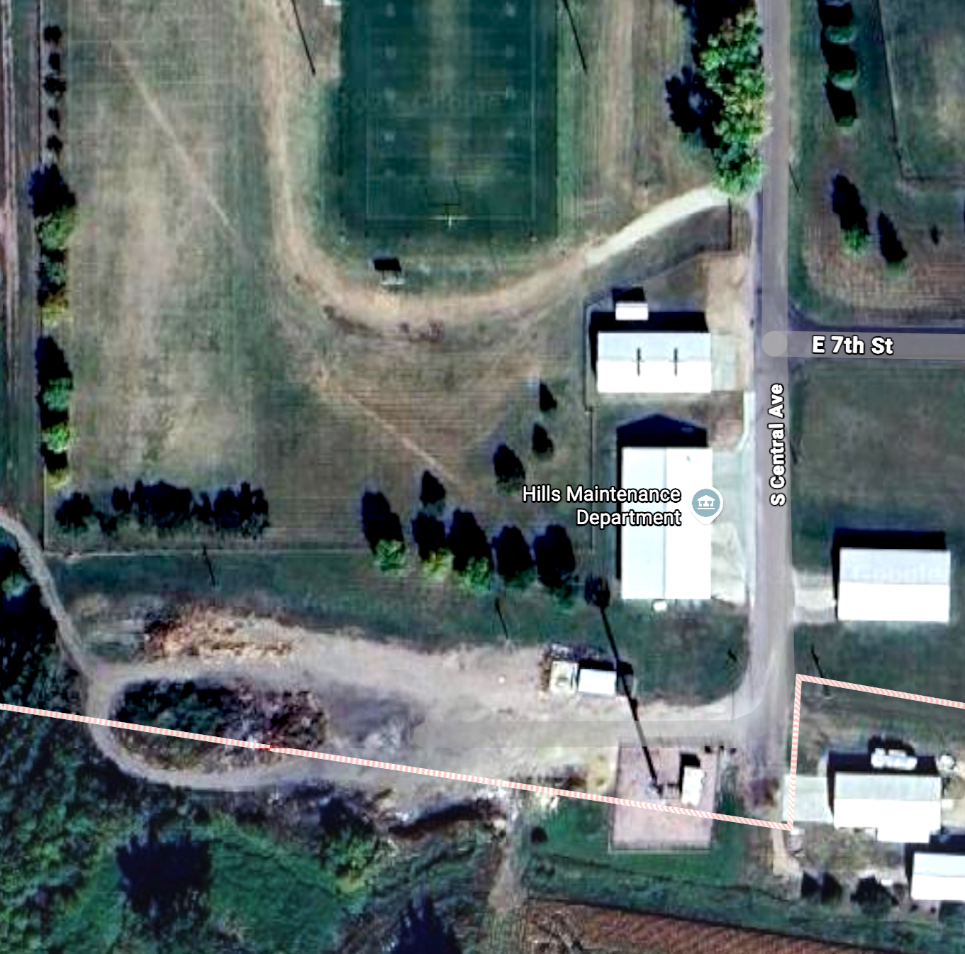 Satellite view of Hills Maintenance Department building located on South Central Avenue near East 7th Street, with surrounding trees, open field, and neighboring structures.