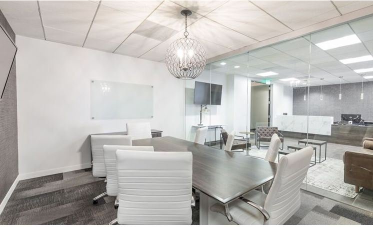 Modern conference room with a large wooden table, white chairs, a glass wall, a whiteboard, a flatscreen TV, and a chandelier.