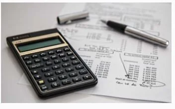 Calculator, pen, and financial documents with charts and graphs on a desk.