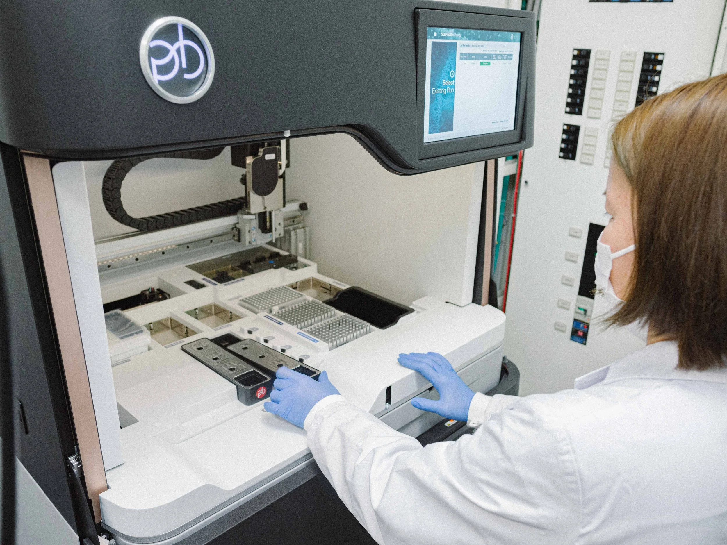 Laboratory technician working with automated equipment, wearing a mask and gloves.
