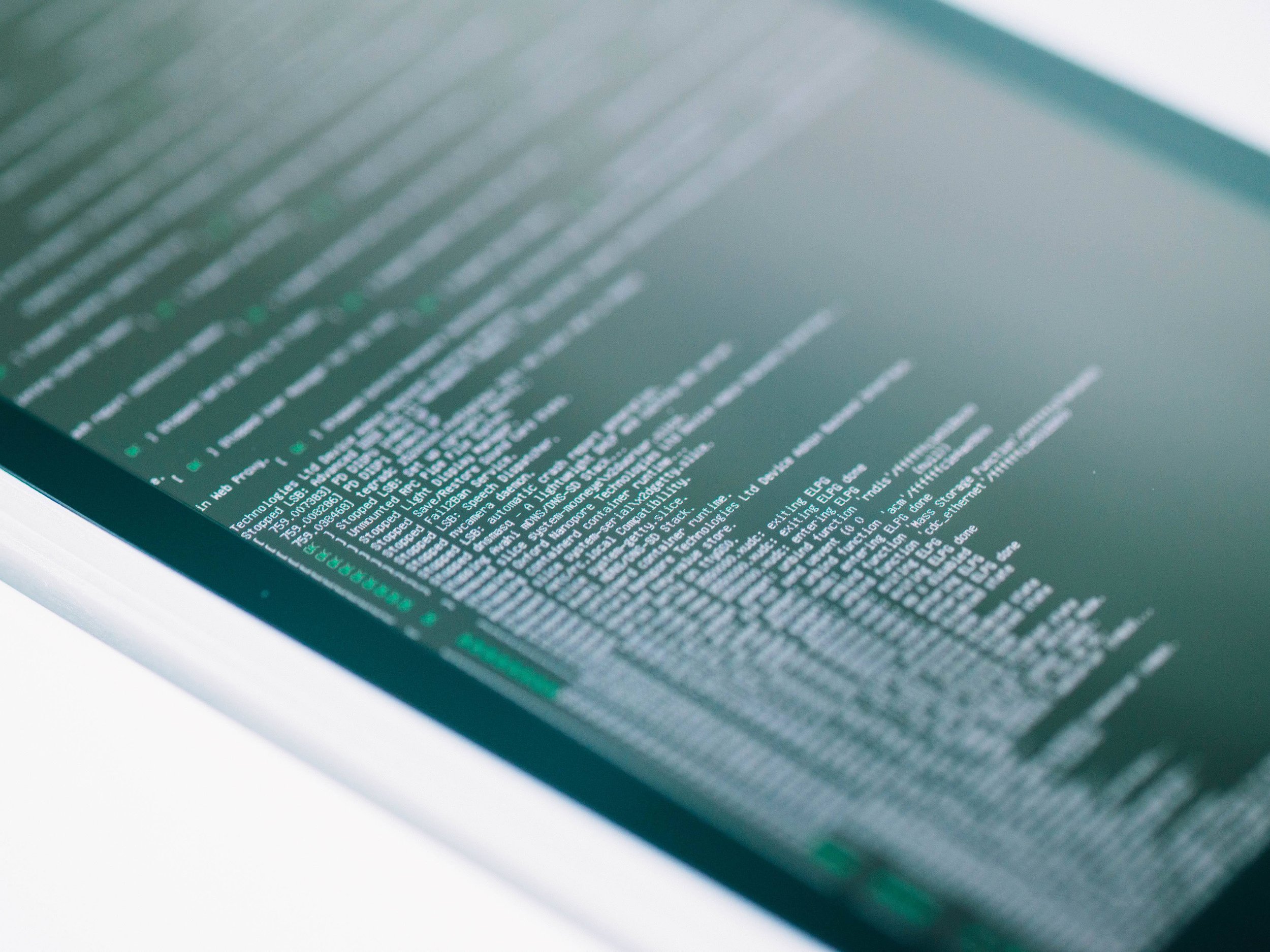 Close-up of a tablet screen displaying lines of green and white code or text on a dark background.