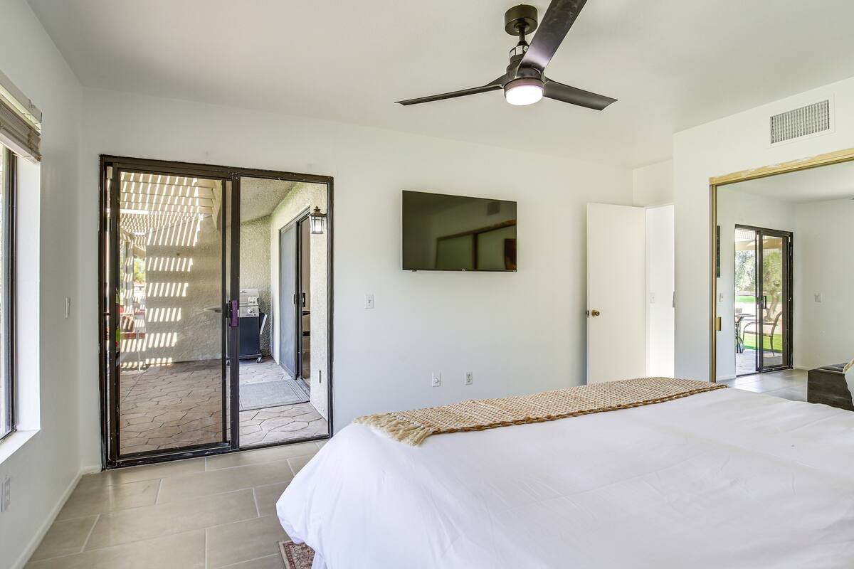 Bedroom with sliding glass door leading to outdoor patio, ceiling fan, wall-mounted TV, and a white bed with a blanket.