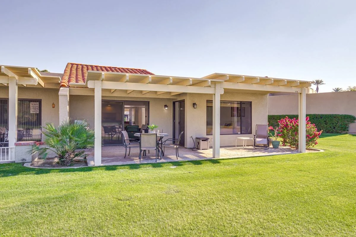 Backyard patio with outdoor dining table, chairs, lounge chairs, and landscaped lawn.
