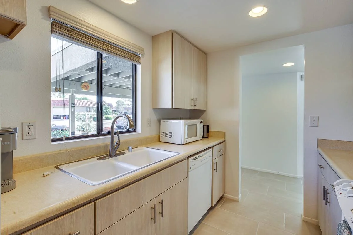 Kitchen with beige counter, white sink, microwave, and cabinets, window with view outside.
