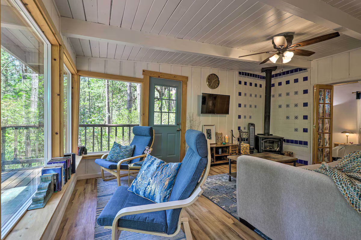 Cozy living room with large windows, wooden accents, a wood stove, and comfortable seating.