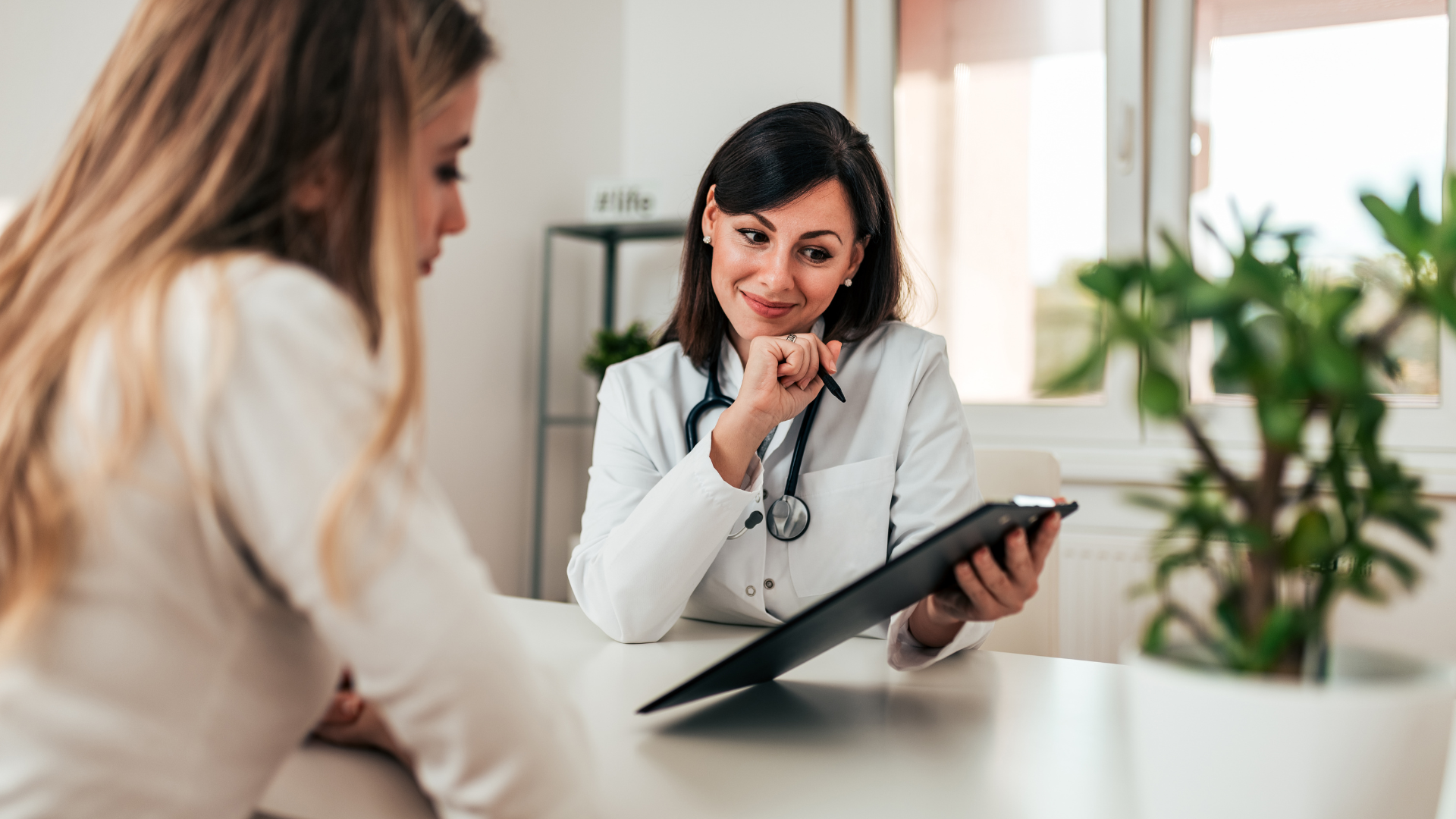Medical professional, woman with stethoscope, discussing with another woman in a clinic or hospital setting, holding a tablet device. One hour nutritionist consultation is included in your Luxury Wellness Experience.