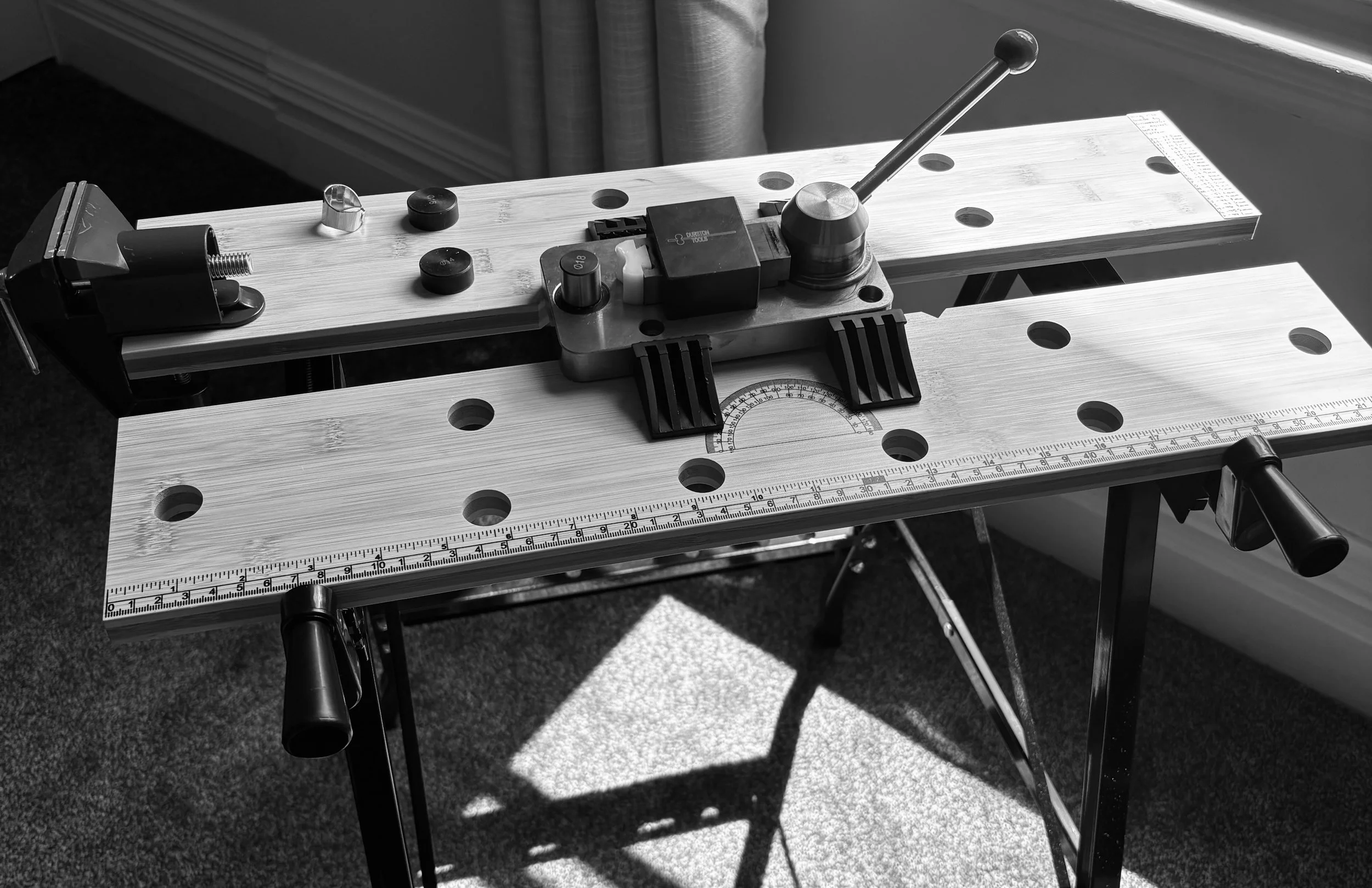 A woodworking workbench with a large ruler, a protractor, and clamps, set in natural light.