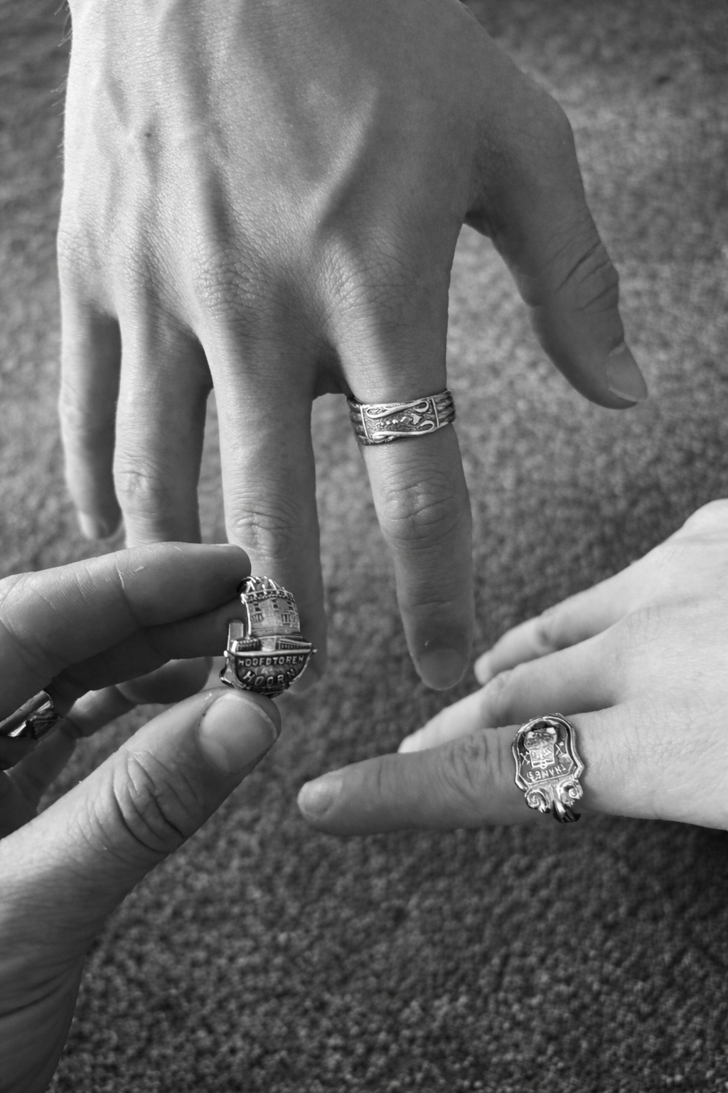 Close-up of three hands with rings, reaching towards each other, on a textured surface.