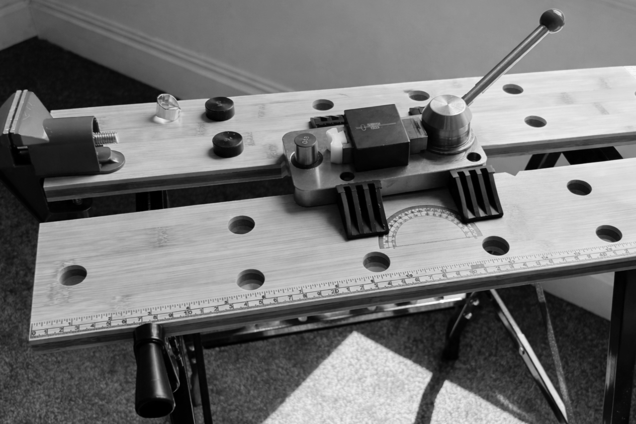A woodworking router table with a guide fence, a fence adjustment knob, and a semi-circular measurement guide, set up in a workshop.