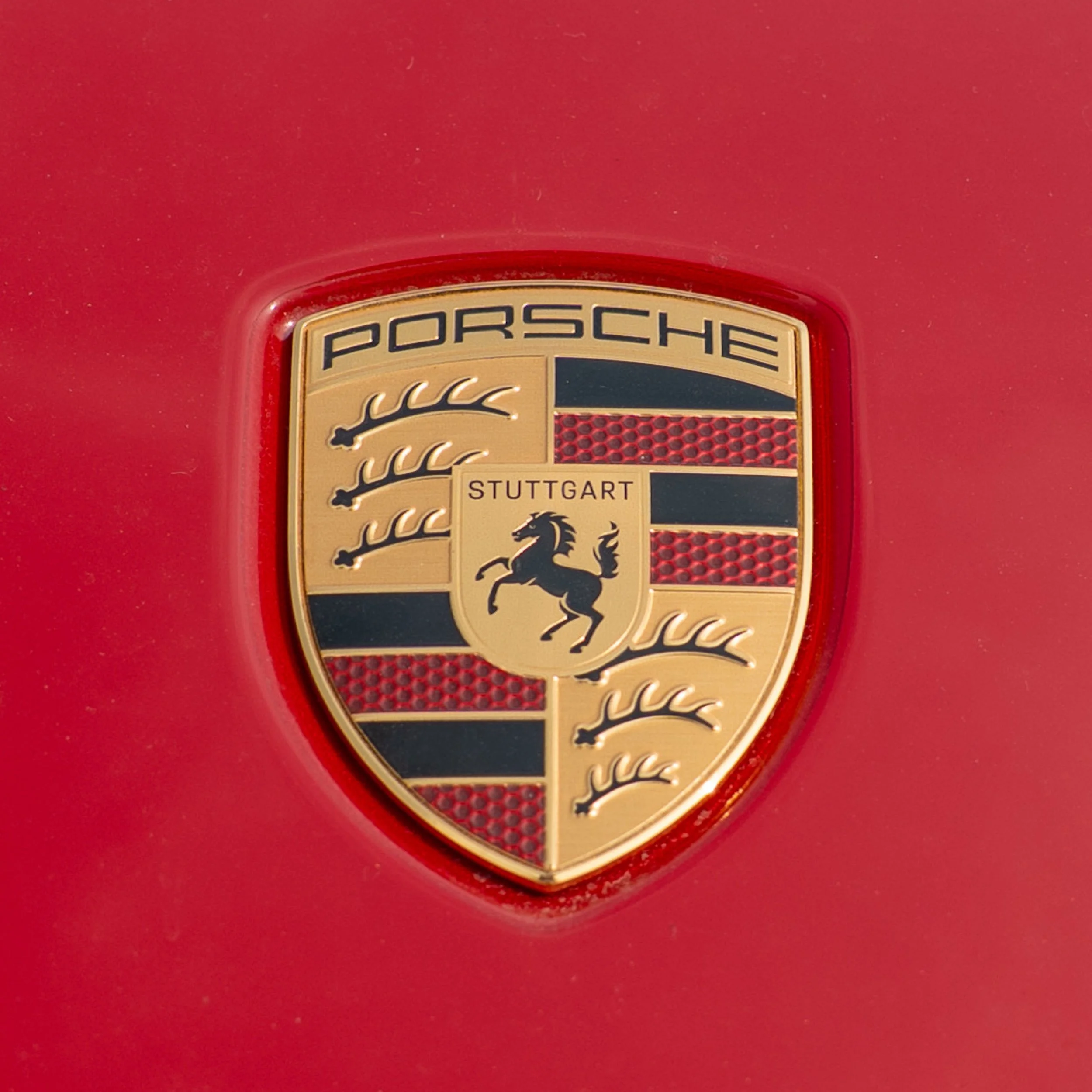 Close-up of a Porsche emblem on a red car, featuring a black horse and red and black stripes, with the words 'Porsche' and 'Stuttgart'.