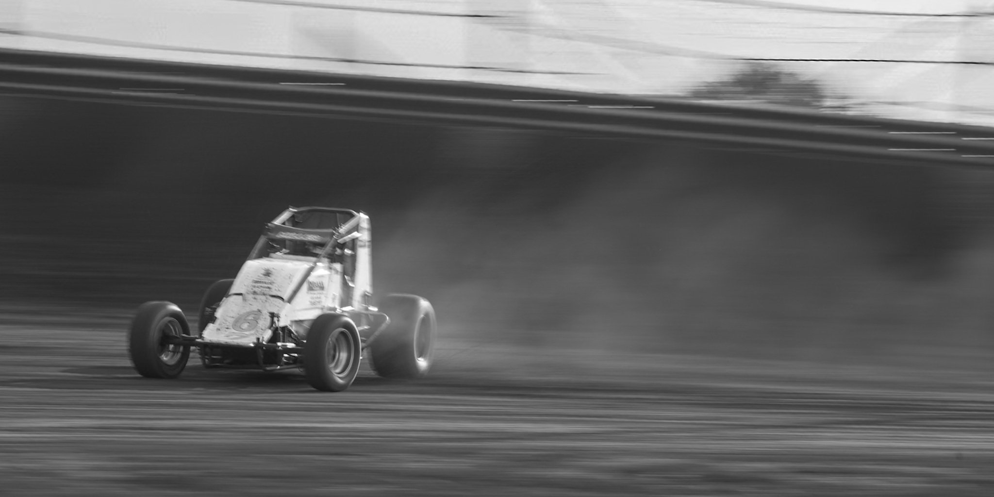 A race car speeding on a track, kicking up dust behind it, in black and white.