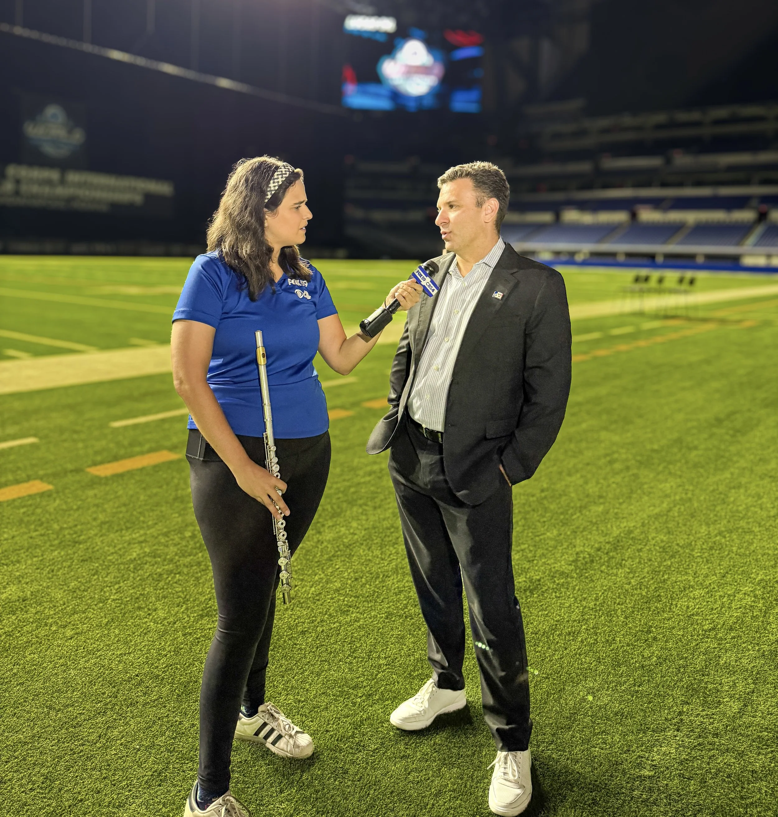 Female news reporter interviewing a male football coach on a football field at night.
