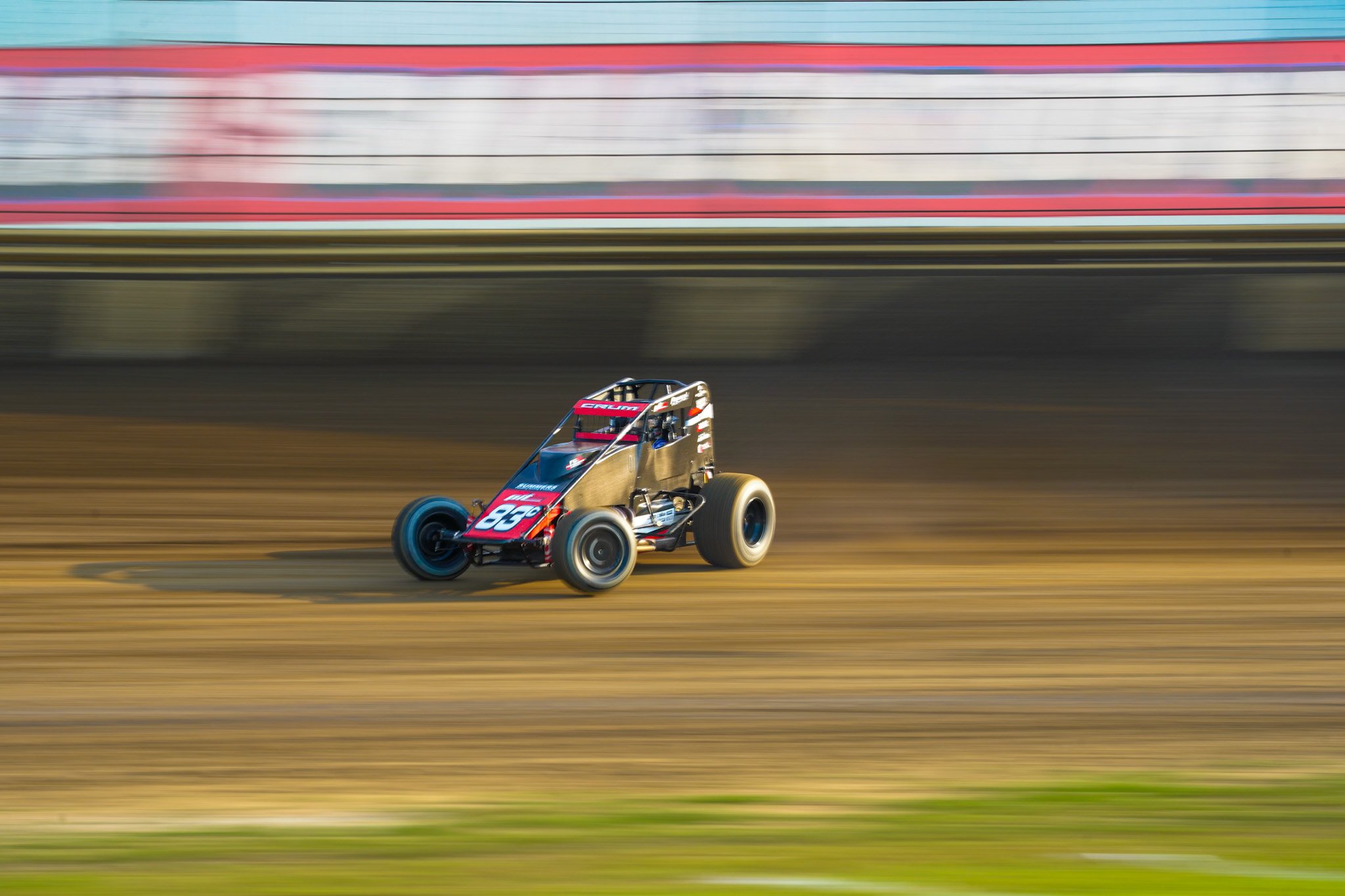 A black and red race car speeding on a dirt race track with a blurred background.