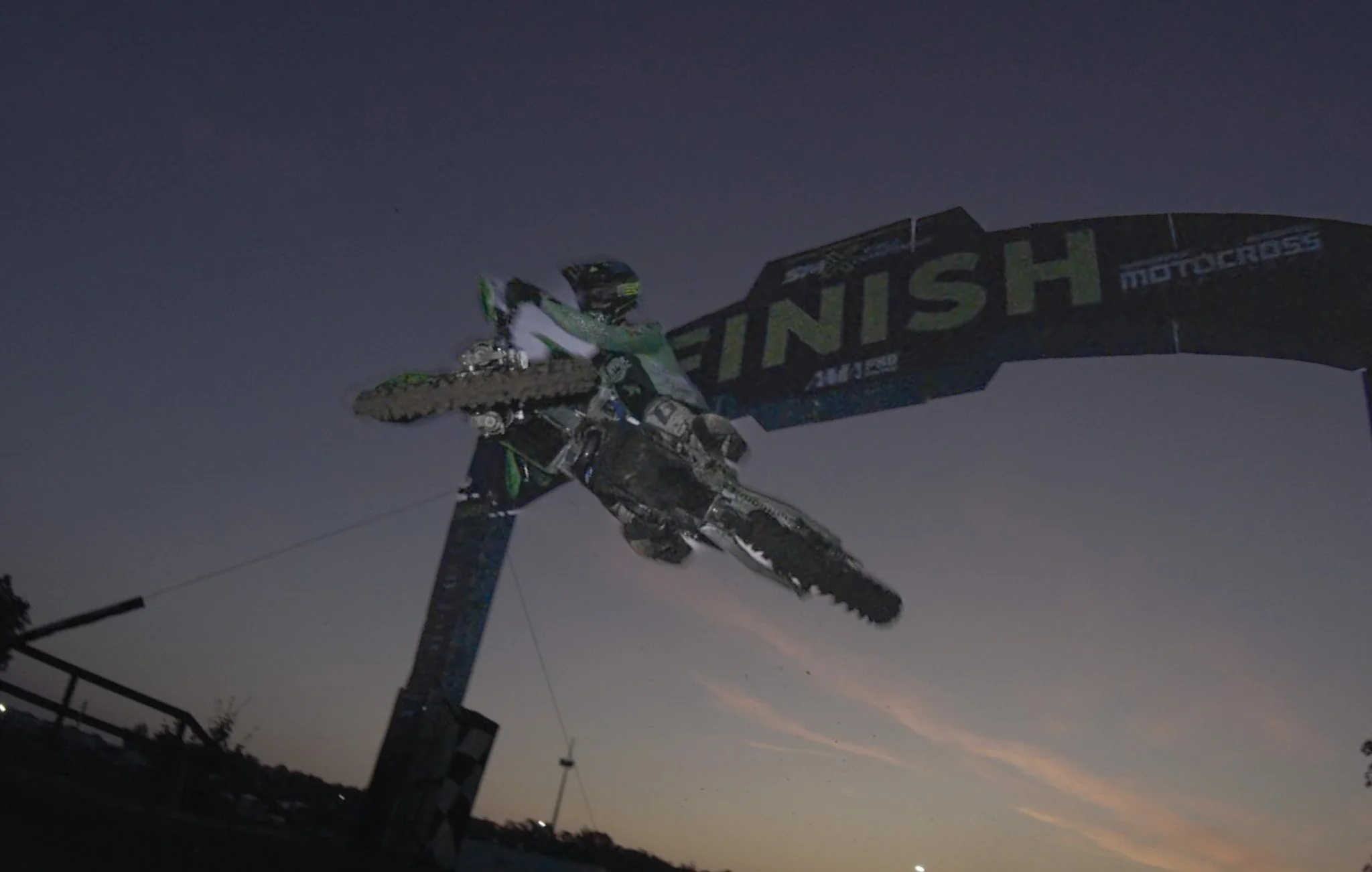 Motocross rider jumping with a 'Finish' banner in the background during dusk.