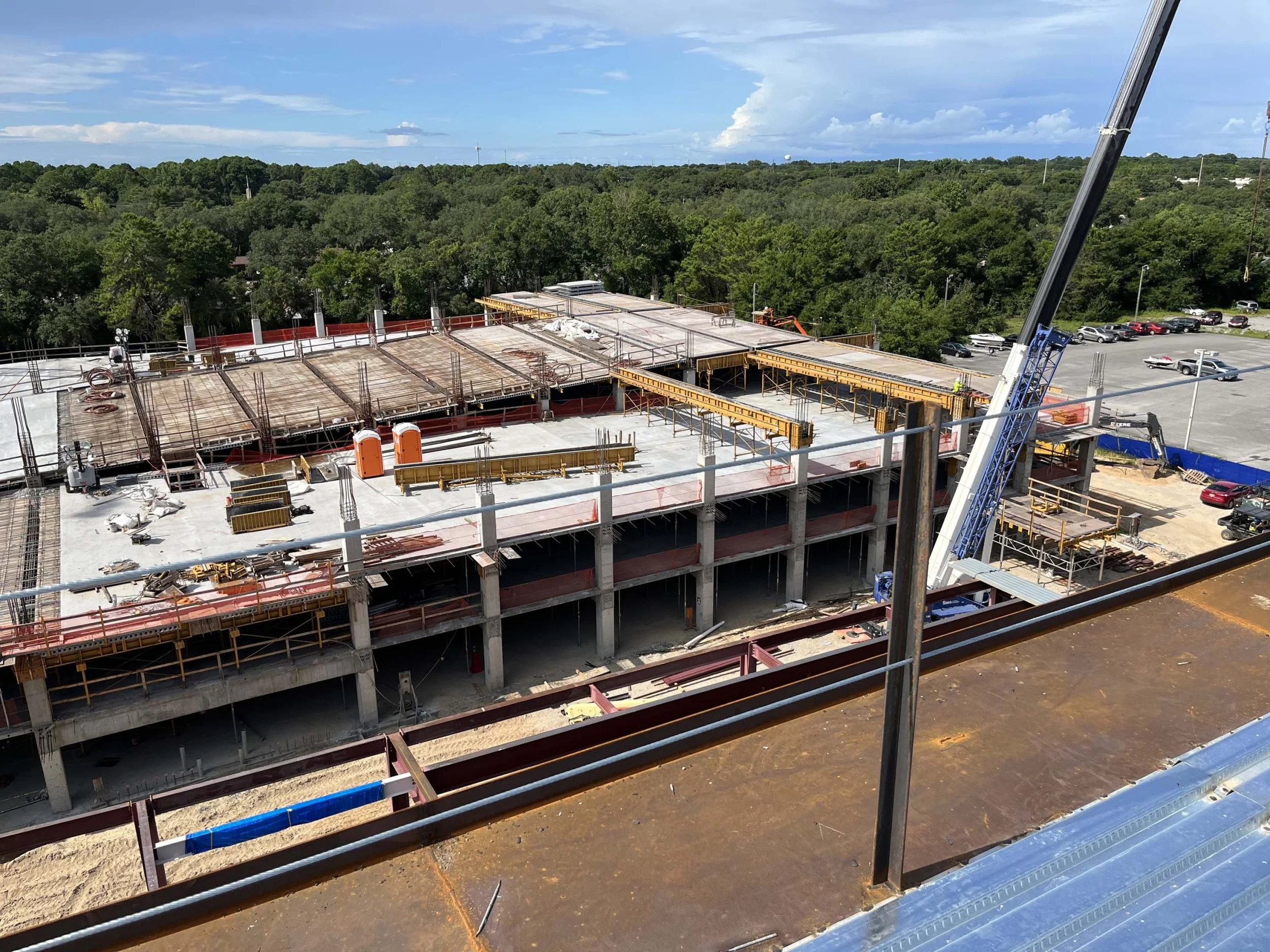 Construction site showing a multi-story building in progress with concrete floors, scaffolding, cranes, and construction workers.