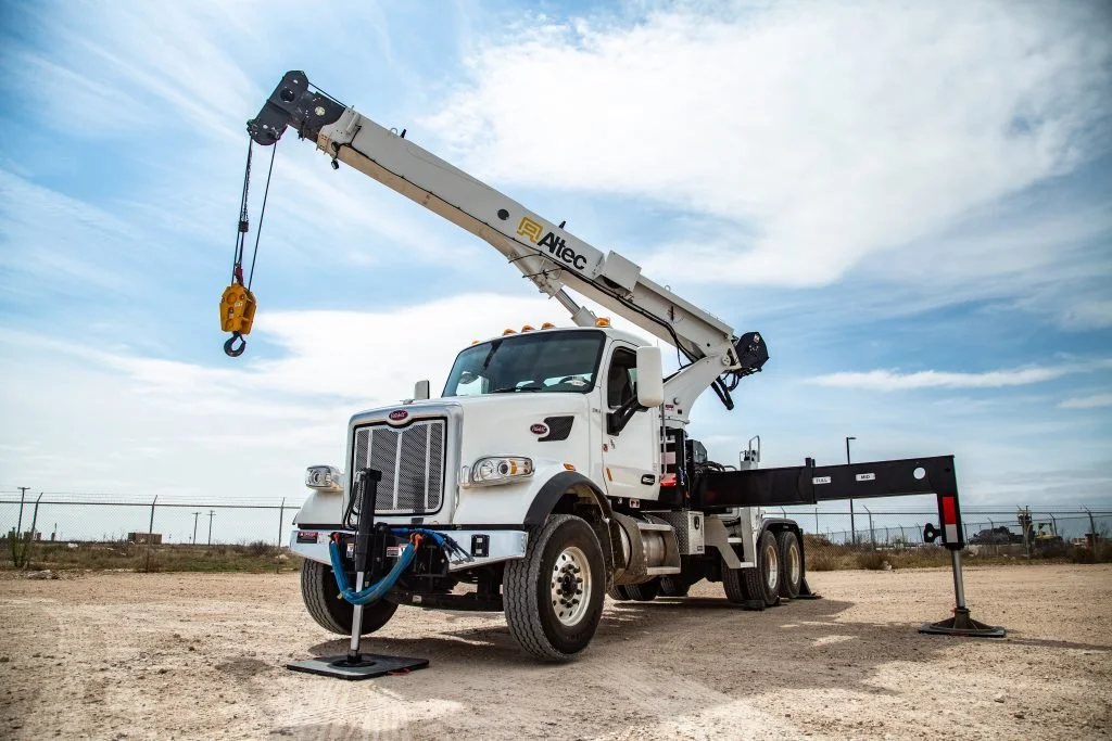 White utility truck with a mounted crane, set on a dirt lot under a partly cloudy sky.