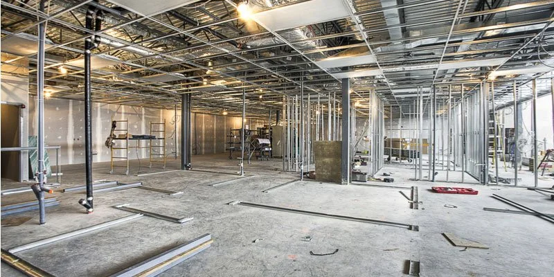 Interior of a building under construction, with metal framing, scaffolding, and construction tools.
