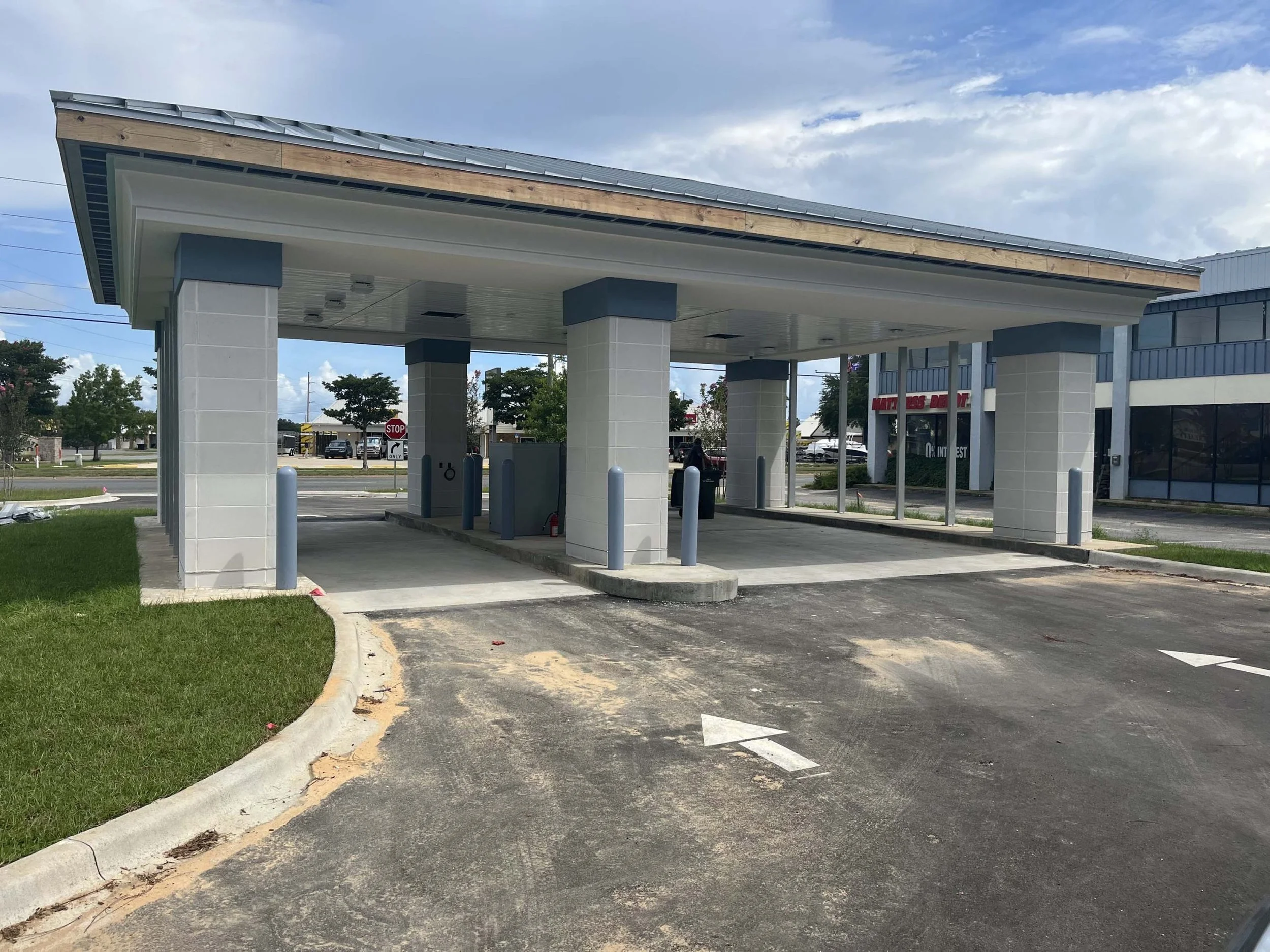 Empty car charging station with three charging units, gray pillars, metal roof, and directional arrows painted on the asphalt.