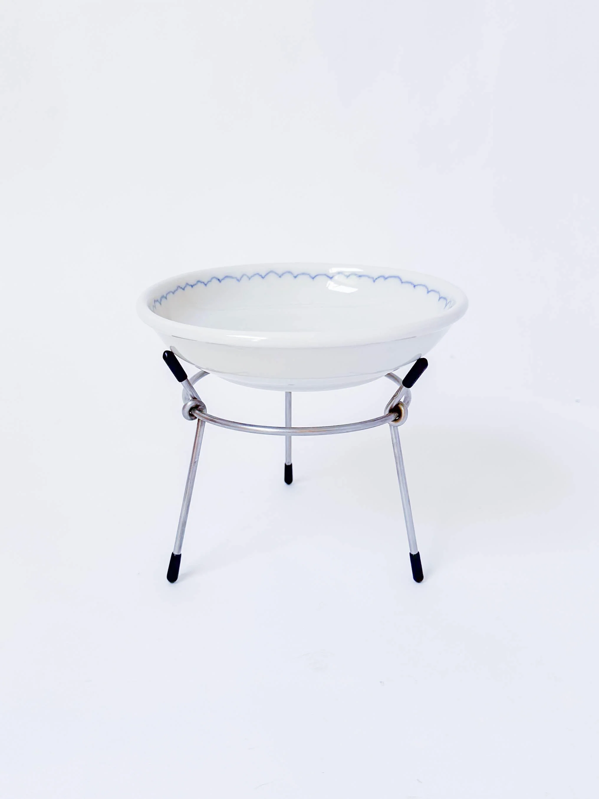A ceramic bowl resting on a metal stand with three legs, against a plain white background.