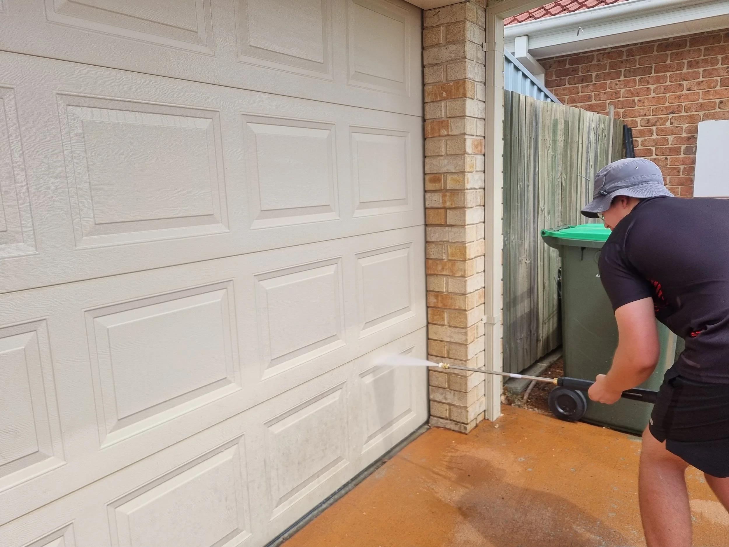 A person cleans house garage with pressure washer.