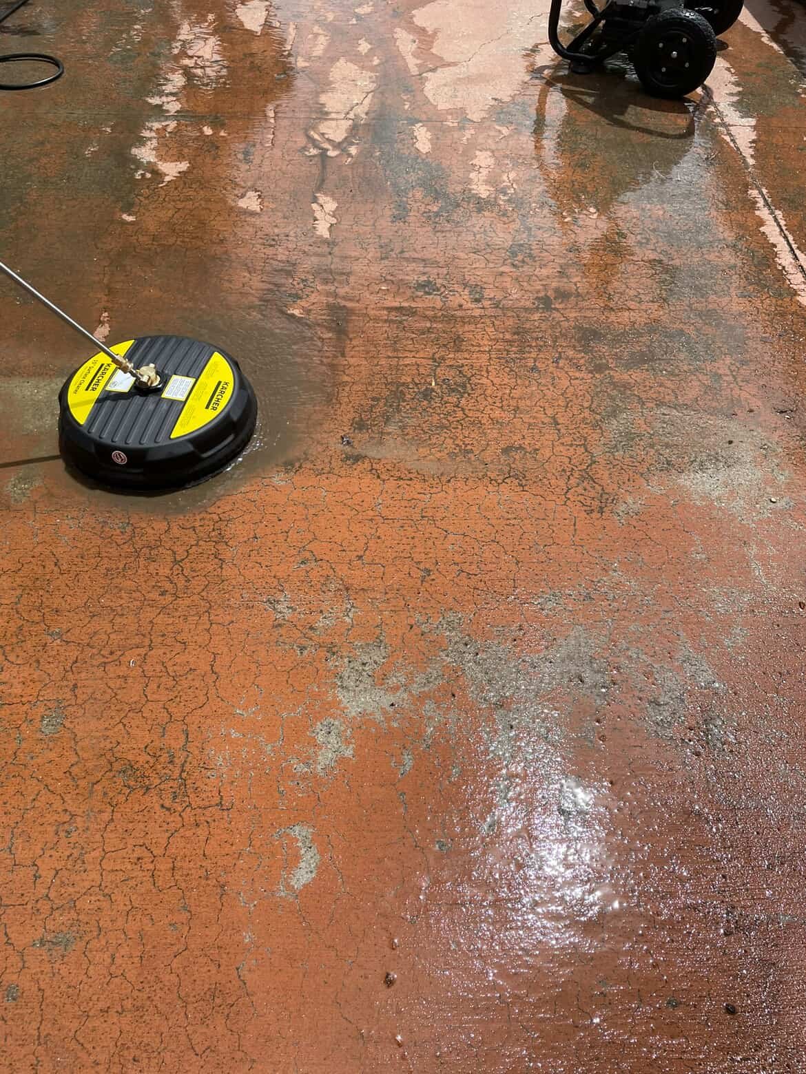 Close-up of an orange concrete floor being cleaned with a floor buffer, showing wet and dry patches.