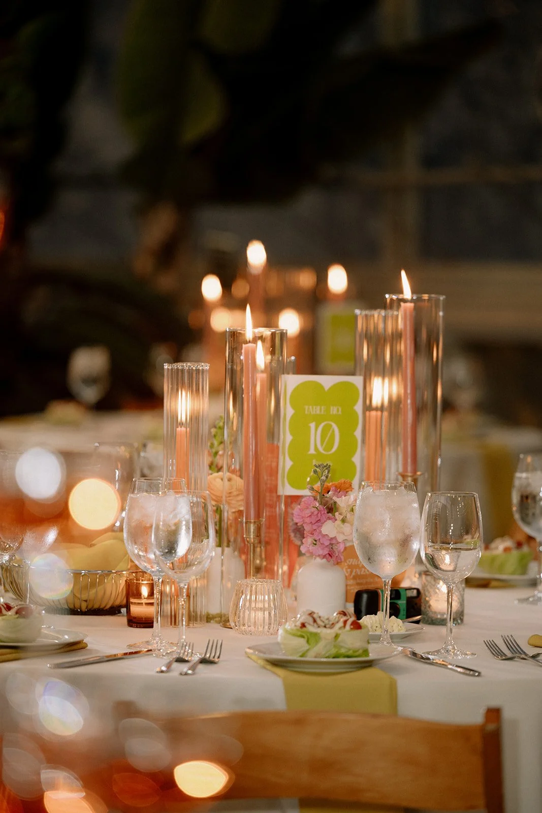 A decorated banquet table with pink candles, floral arrangements, glassware, and a table number card for a 10th birthday celebration.