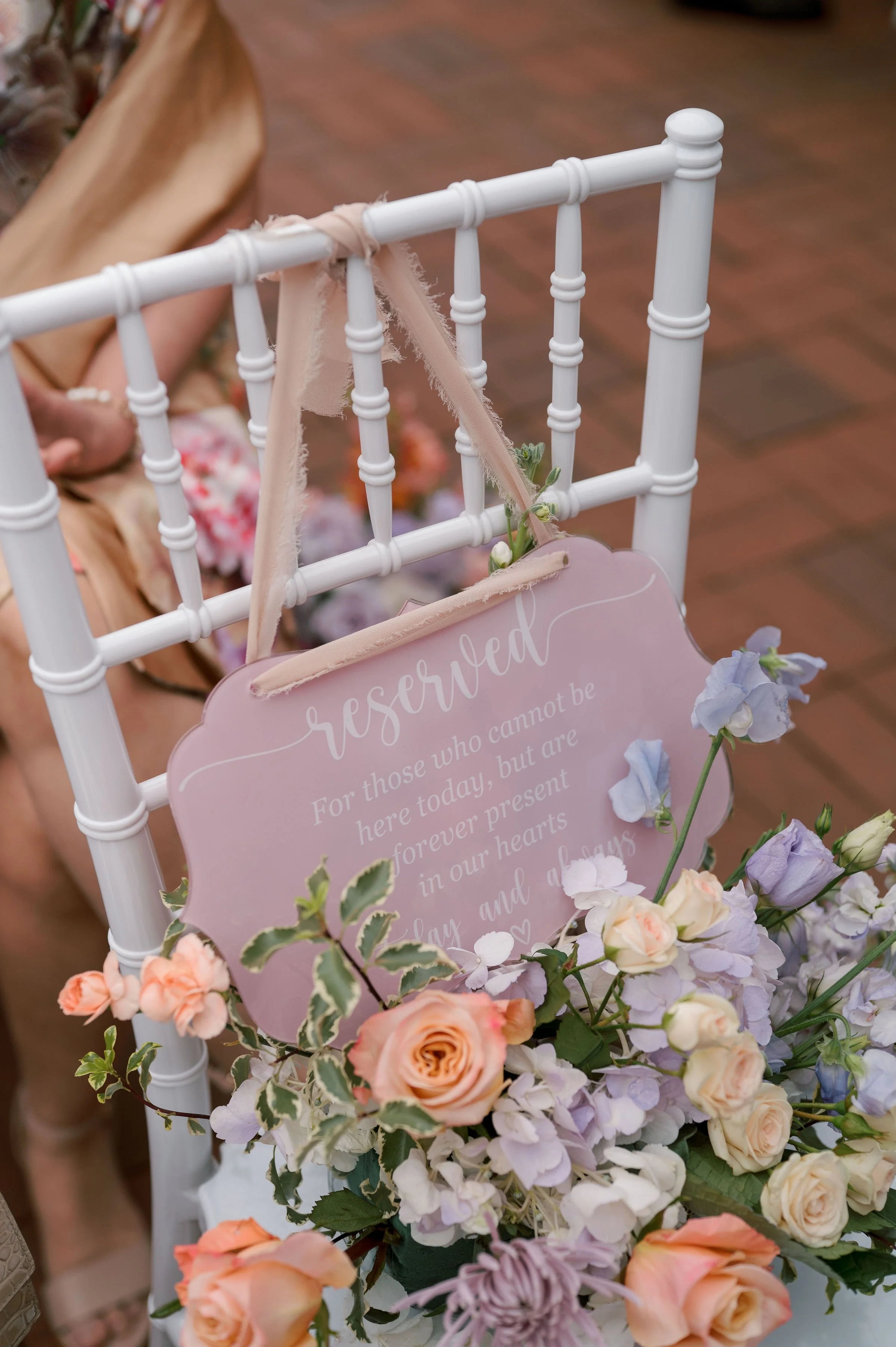 A decorative flower arrangement with pastel-colored roses, hydrangeas, and greenery surrounding a light pink reservation sign on a white chair at a wedding or event.