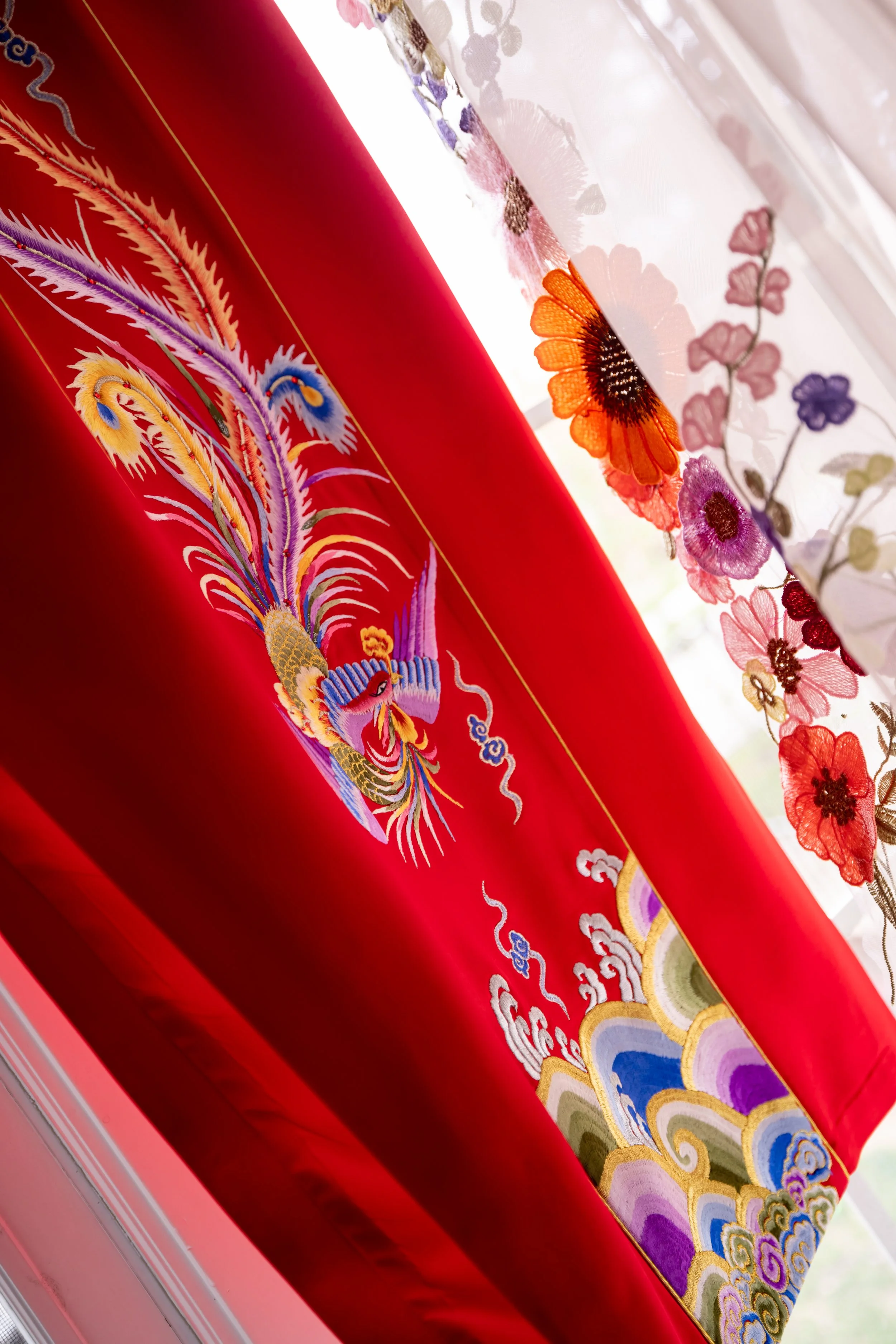 Close-up of colorful embroidered fabric featuring a phoenix design on the red section and floral embroidery on the white sheer fabric layered on top.