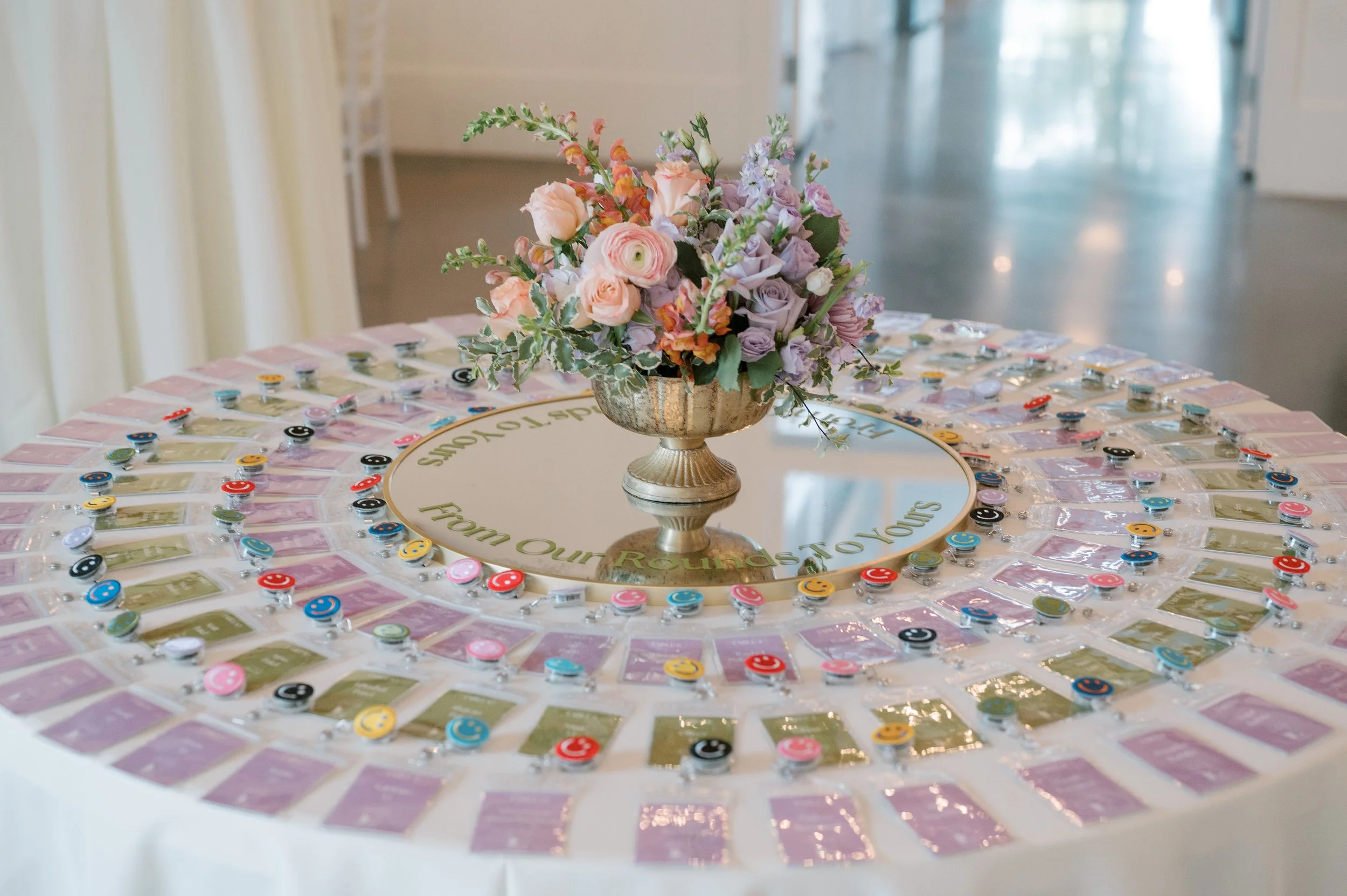 A round table with a flower centerpiece and an arrangement of game pieces and cards around the edge.