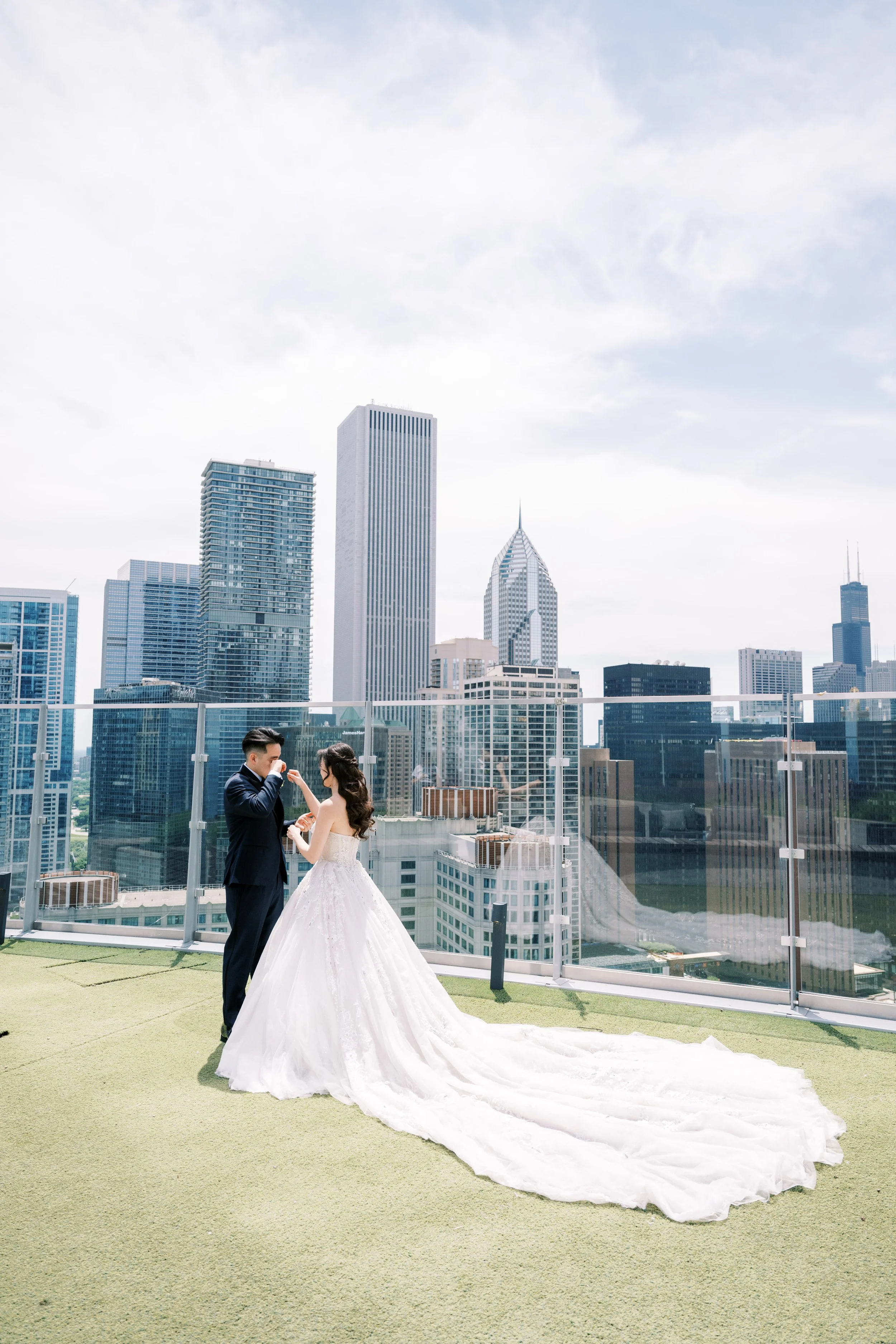 A bride and groom holding hands and looking at each other on a rooftop with a city skyline in the background.
