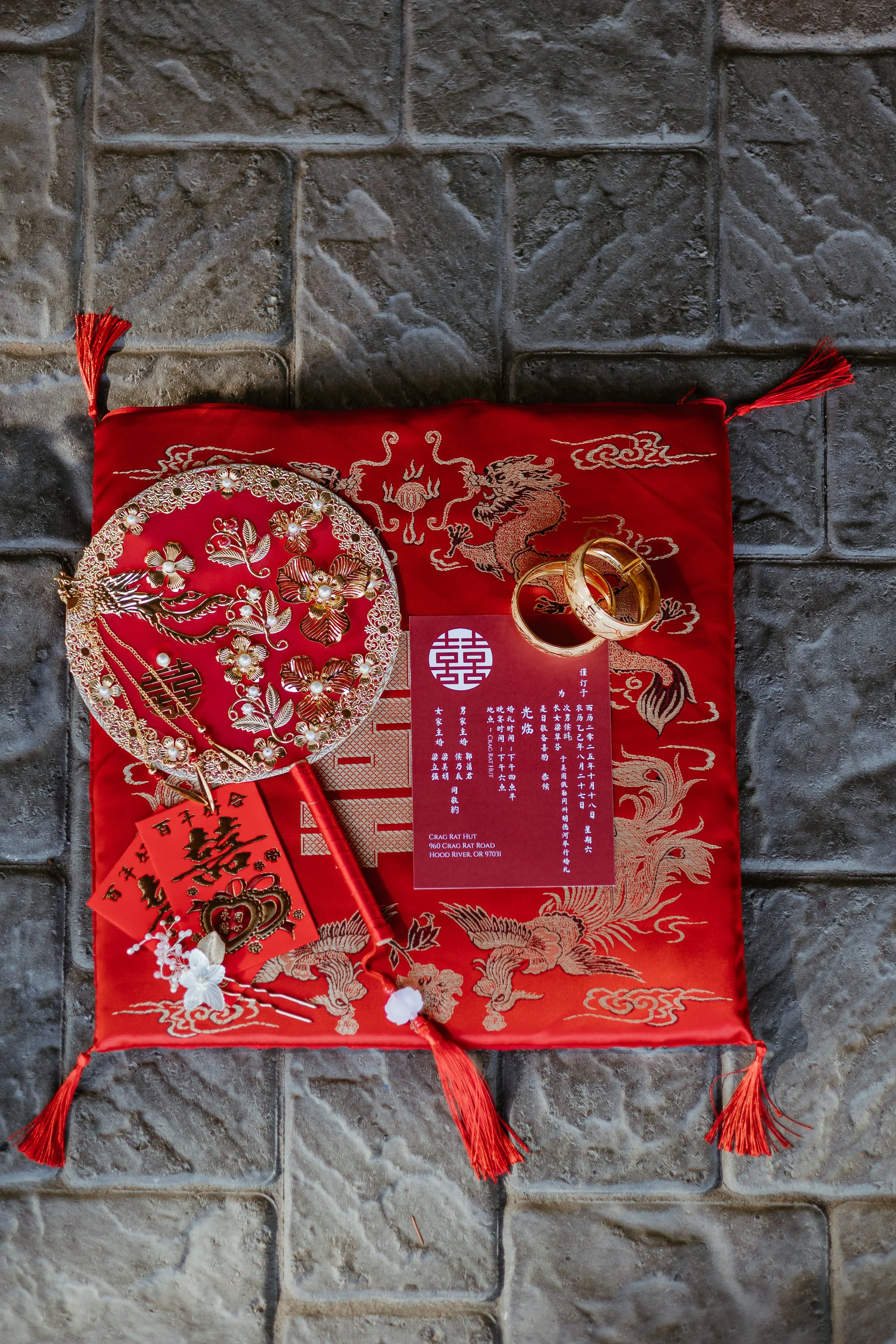 Decorative red silk pouch and gold rings on a red and gold embroidered cloth with Chinese symbols and a dragon design, placed on a tiled stone floor.