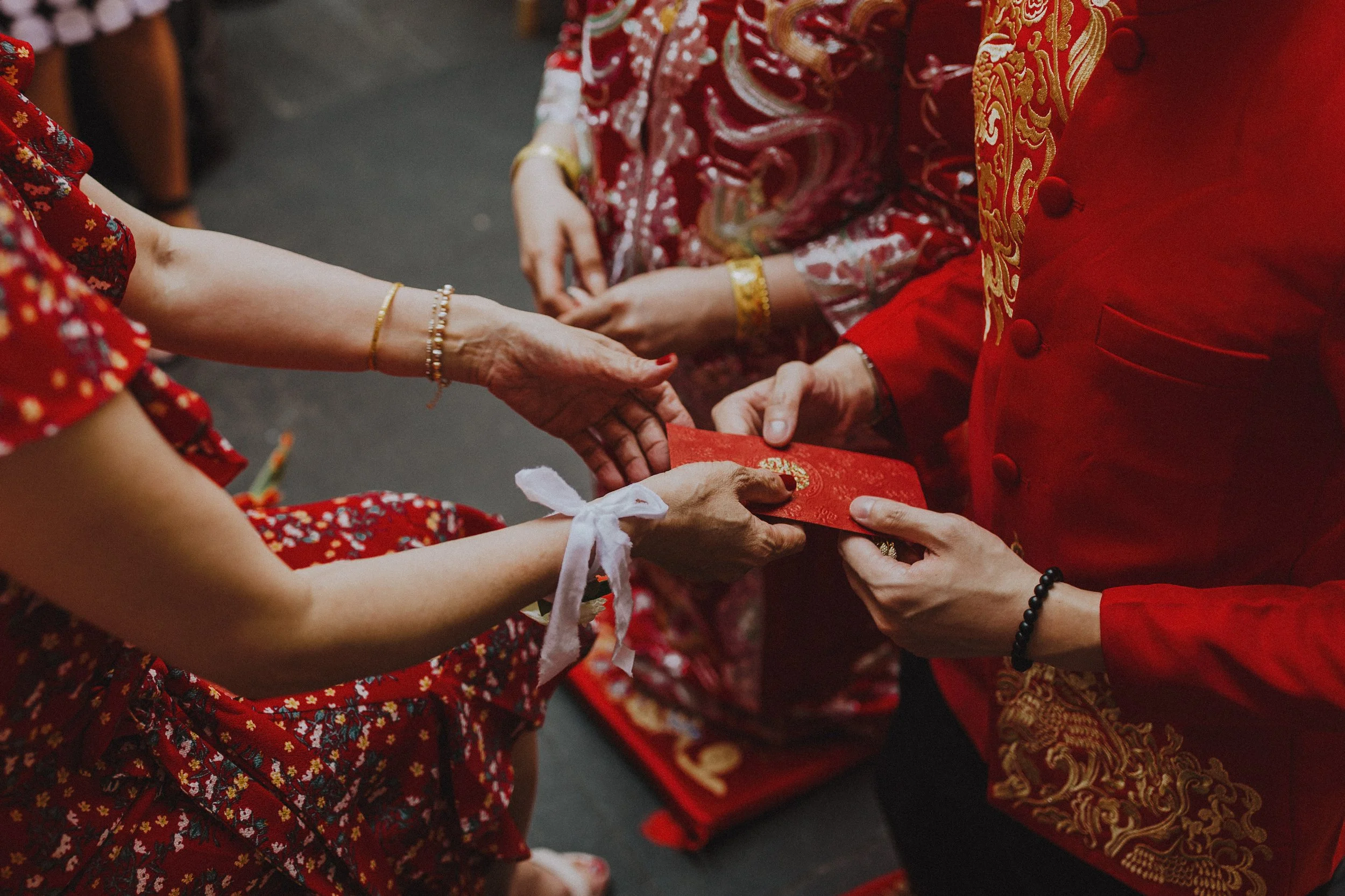 People exchanging red envelopes during a celebration, dressed in traditional red and gold attire.