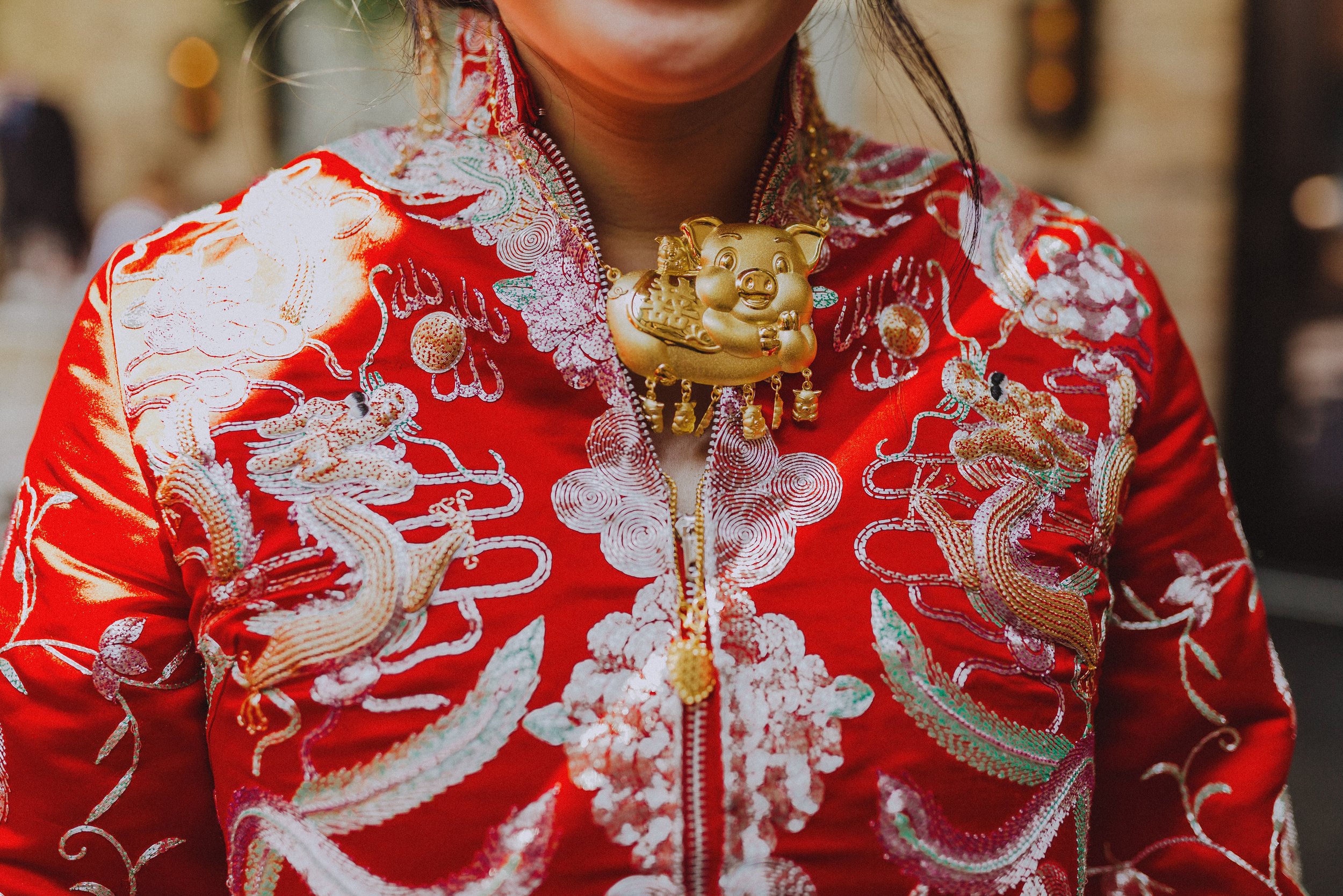 Close-up of a woman wearing a red traditional Chinese dress with intricate embroidery and a gold pig-shaped necklace with dangling ornaments.