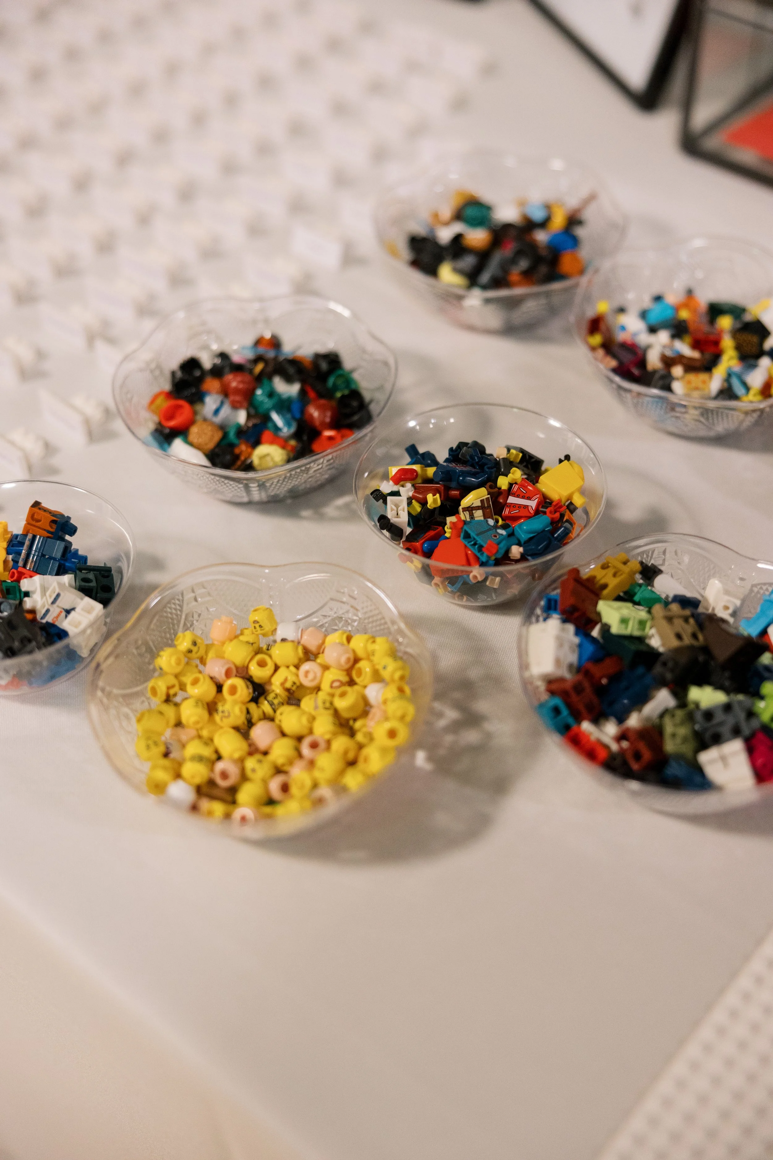 Several clear bowls filled with various colorful LEGO bricks on a white table.
