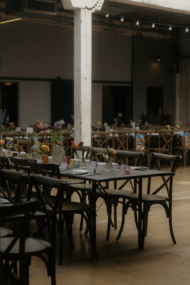 Decorated banquet tables with flowers and table settings in a dimly lit event space.