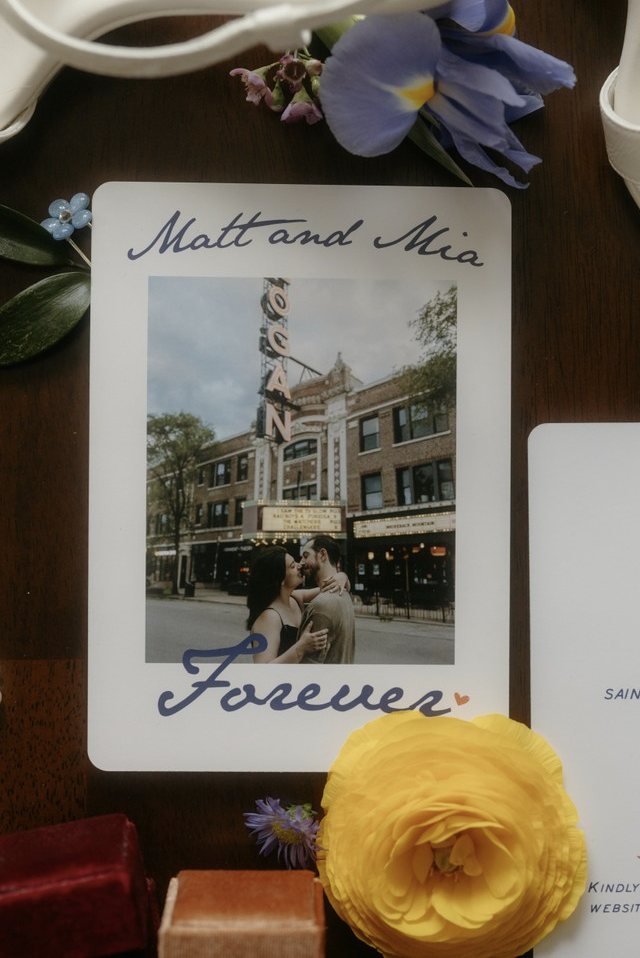 A printed tribute with a photo of a couple in front of a theater marquee that reads 'Orient' and the words 'Matt and Mia' and 'Forever' written on it. The tribute is decorated with purple and yellow flowers.