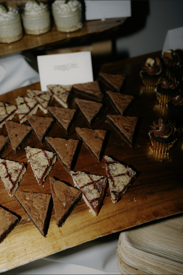 Assorted dessert sandwiches and cupcakes on a wooden serving board at a dessert table.