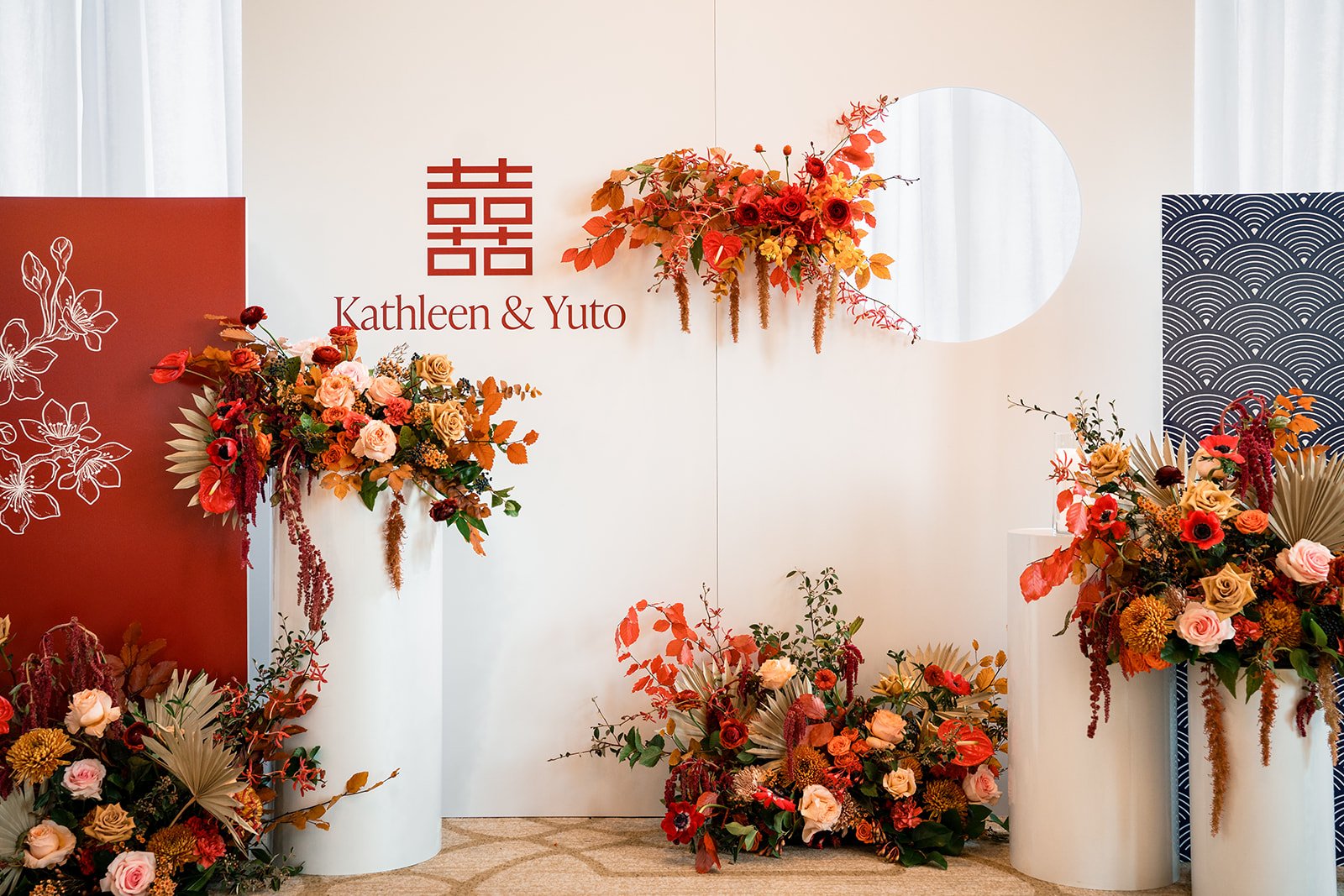 Wedding display with floral arrangements, a white backdrop with the names Kathleen and Yuto, and decorative elements.
