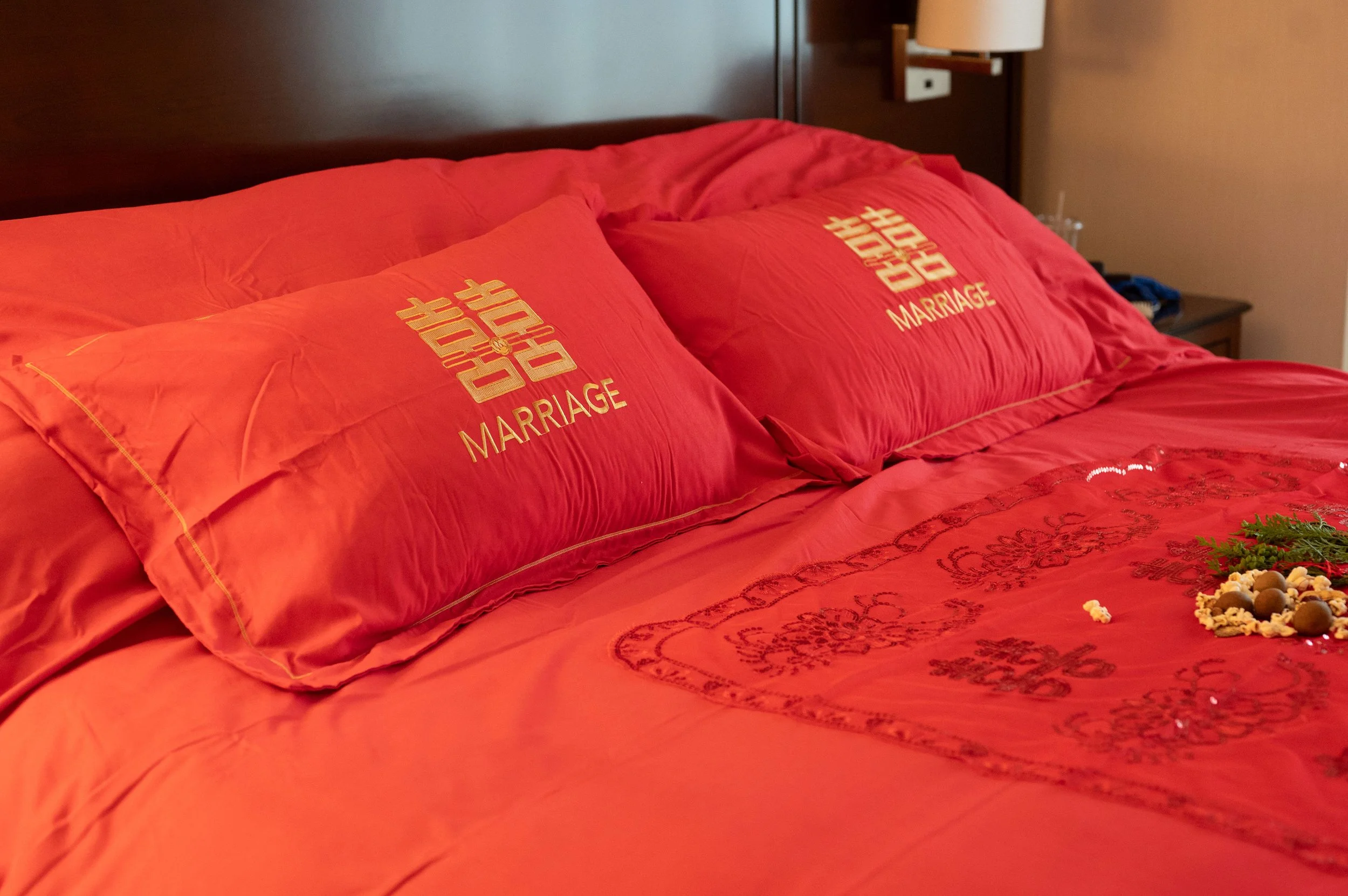 A bed with red bedding and pillows that have 'Just Married' embroidered on them, in a bedroom setting.