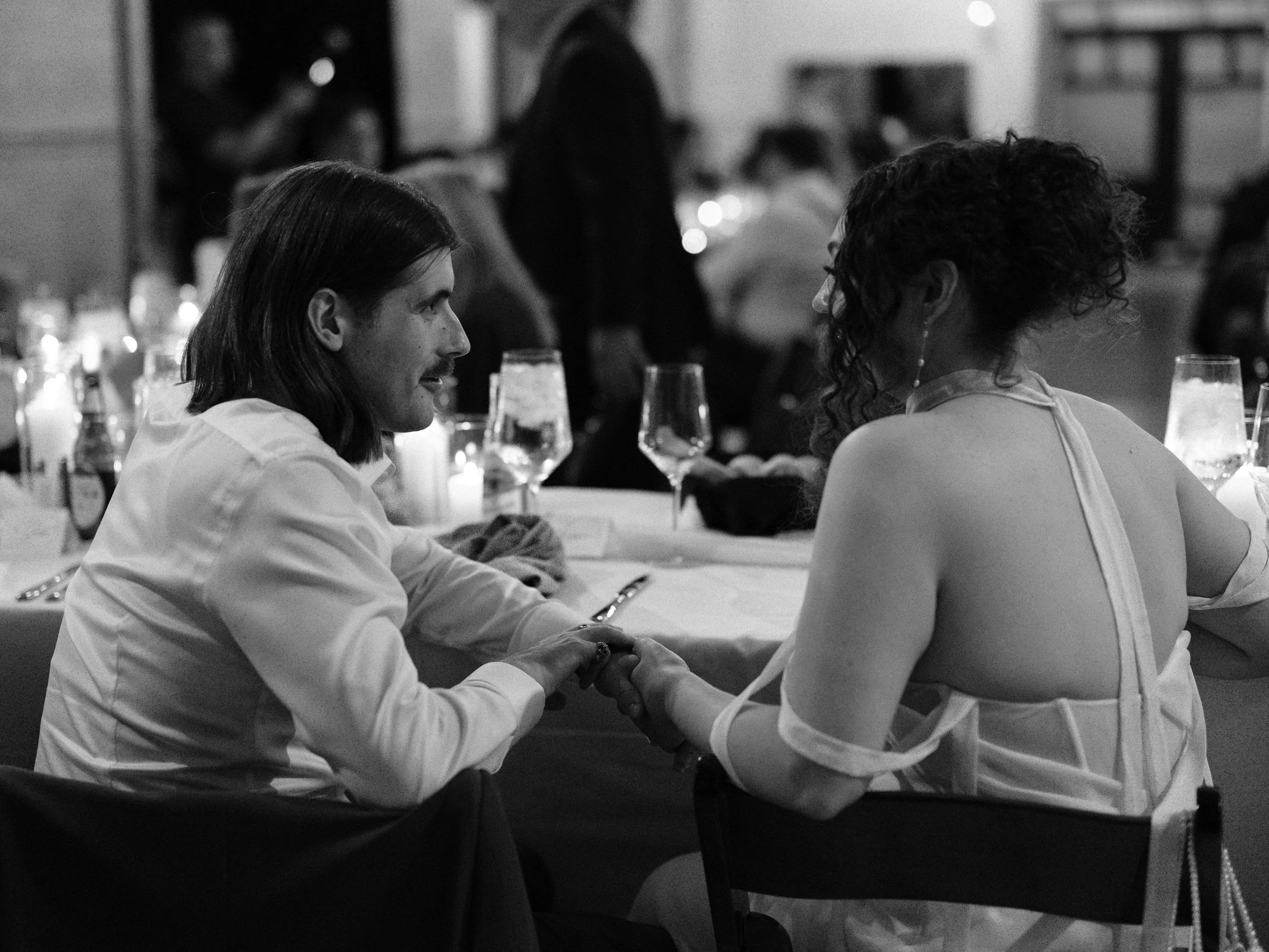A man and woman holding hands at a formal dinner event, in a black and white photo.