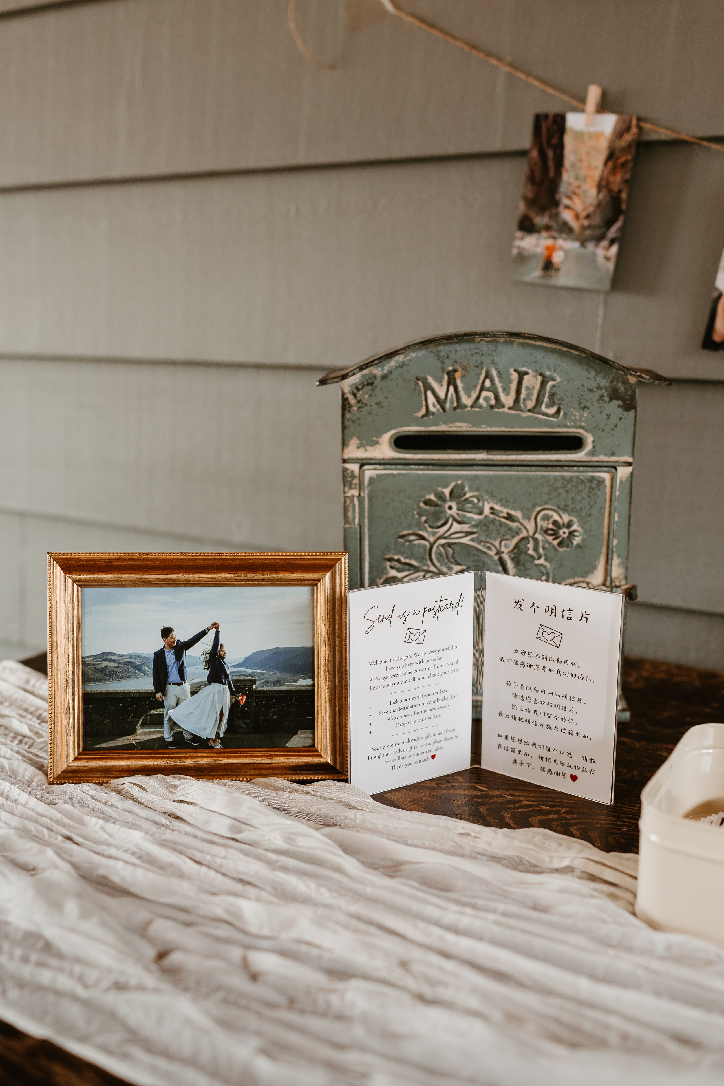 A vintage mailbox with a floral design and the word 'MAIL' on it, plus a framed photograph of a couple dancing outdoors, a postcard, and some note cards on a beige fabric surface.