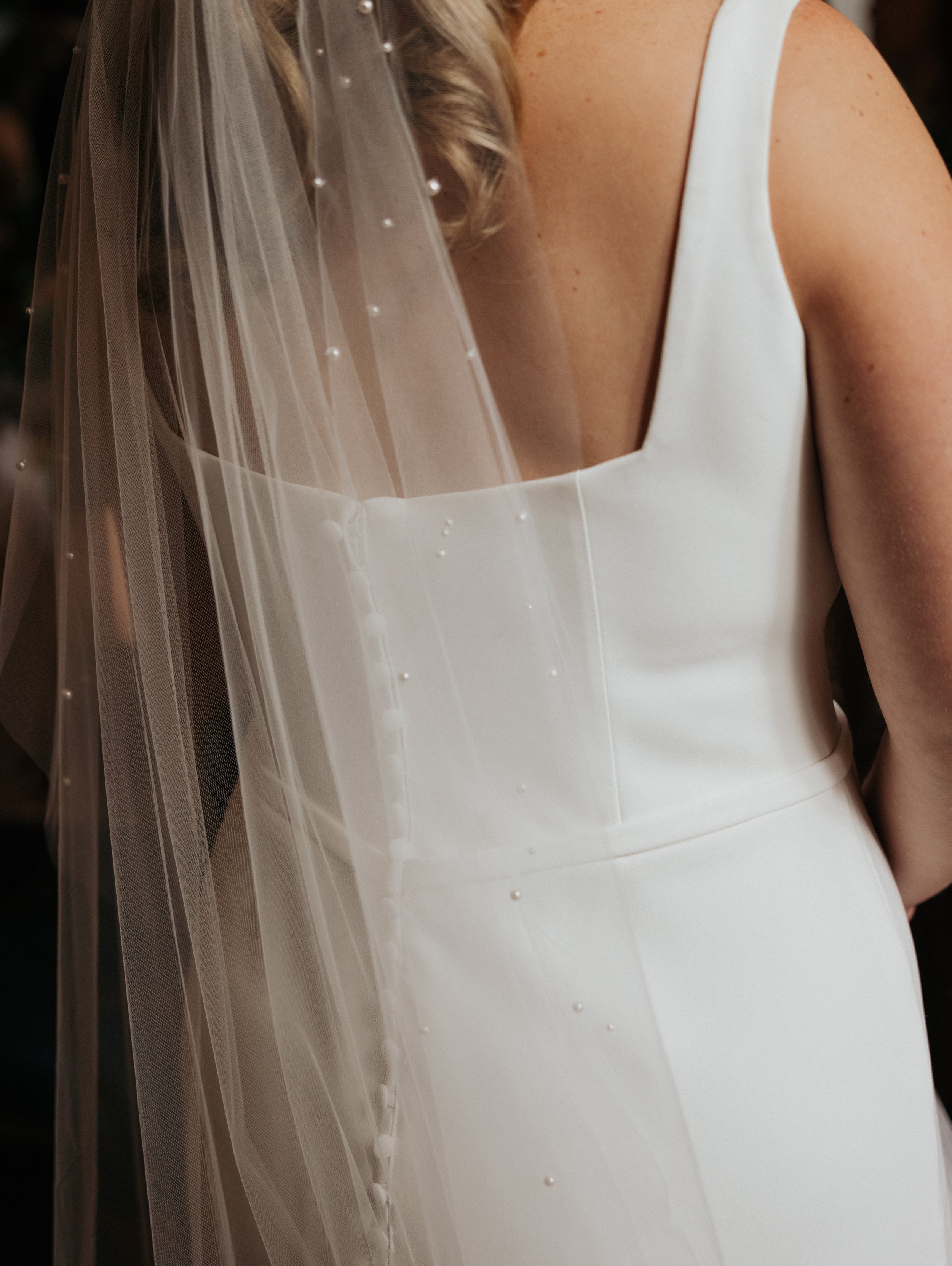 Close-up of a woman in a white wedding dress with a sheer veil decorated with small pearls.