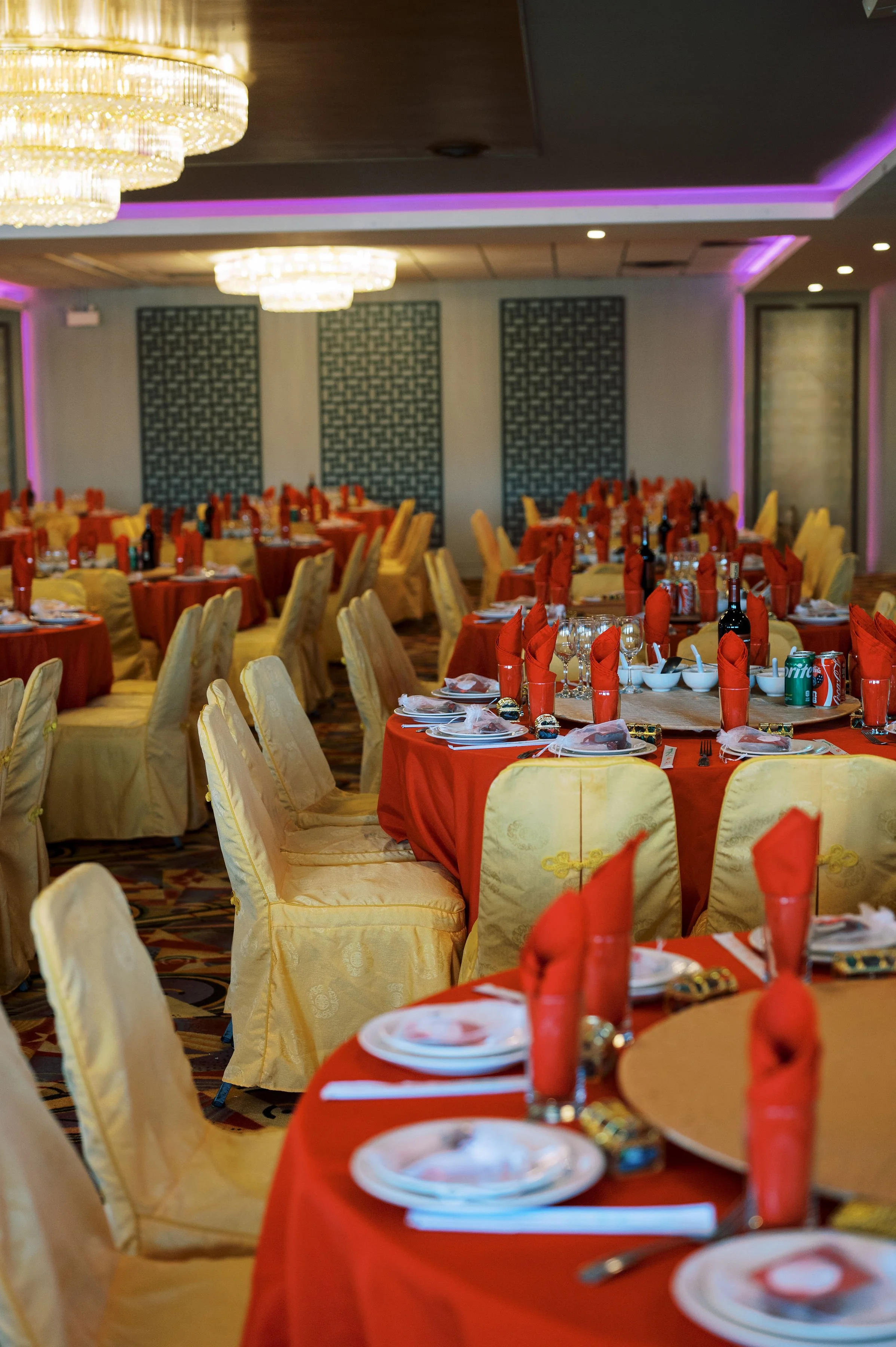 Elegant banquet hall decorated with gold and red table settings, beige chairs, and large chandeliers hanging from the ceiling.