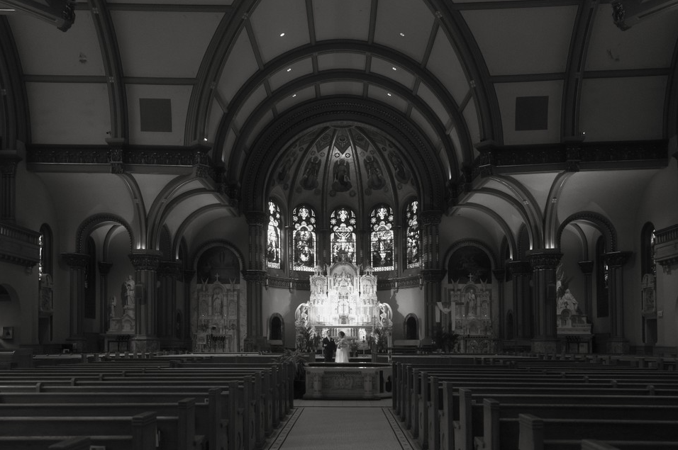 Interior of a church with an ornate altar, stained glass windows, and pews.